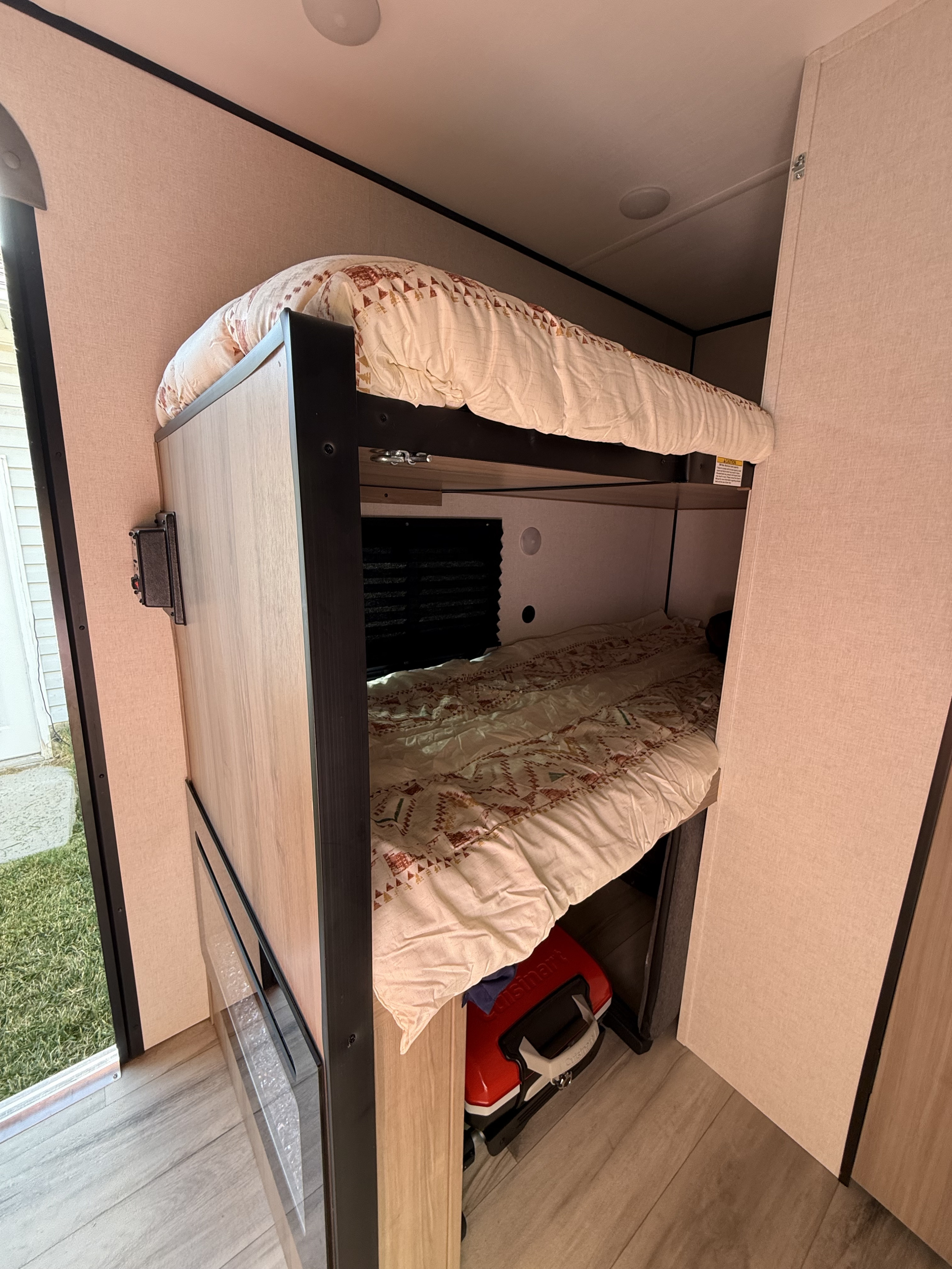 Cozy bunk beds in an RV rental interior with patterned bedding. Glimpse of the outdoors. Ideal for family camping.. Keystone RV Coleman 2025