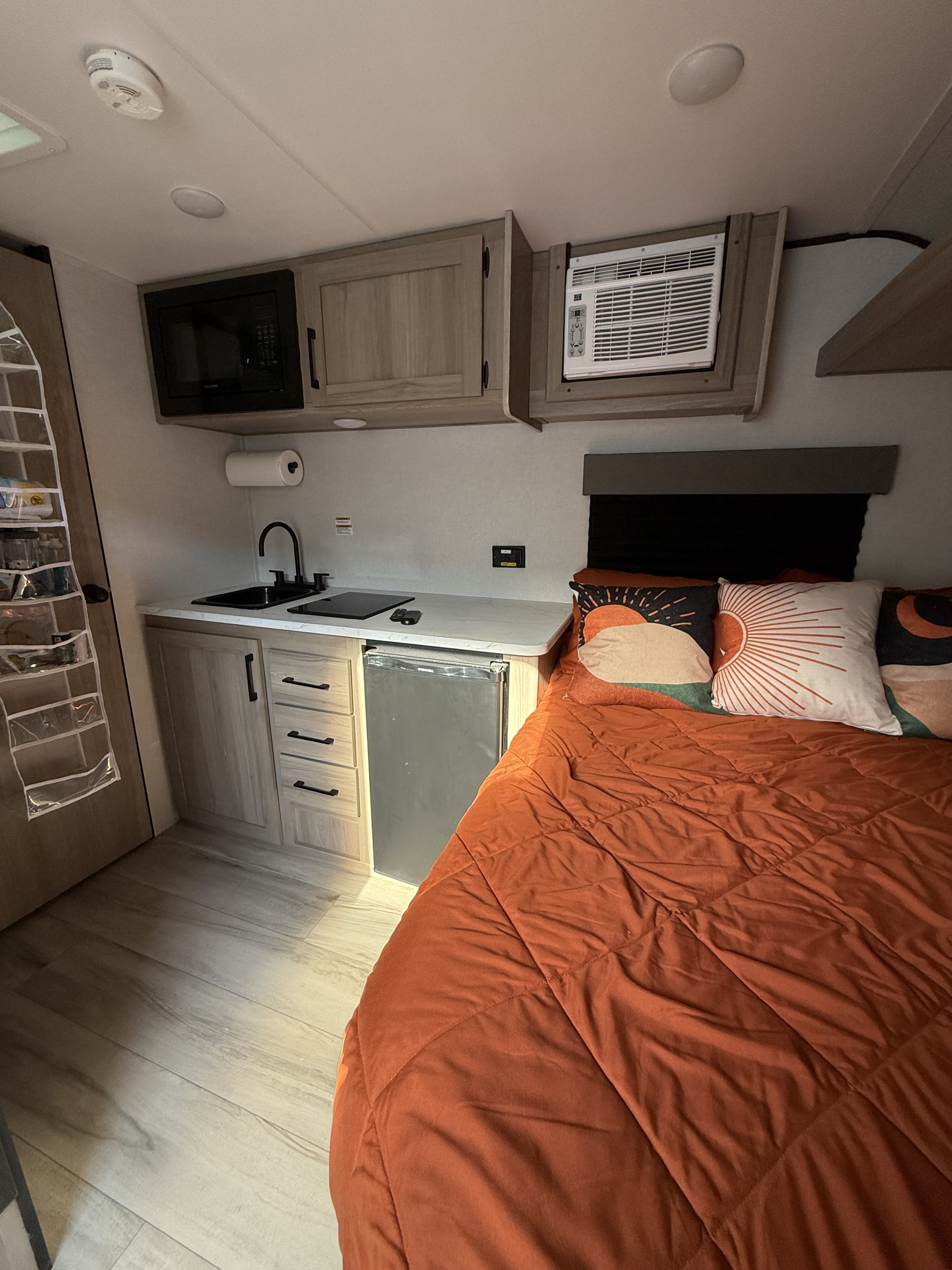This RV rental offers a compact kitchen, comfortable bed with warm orange bedding, AC unit, and practical storage solutions.. Keystone RV Coleman 2025