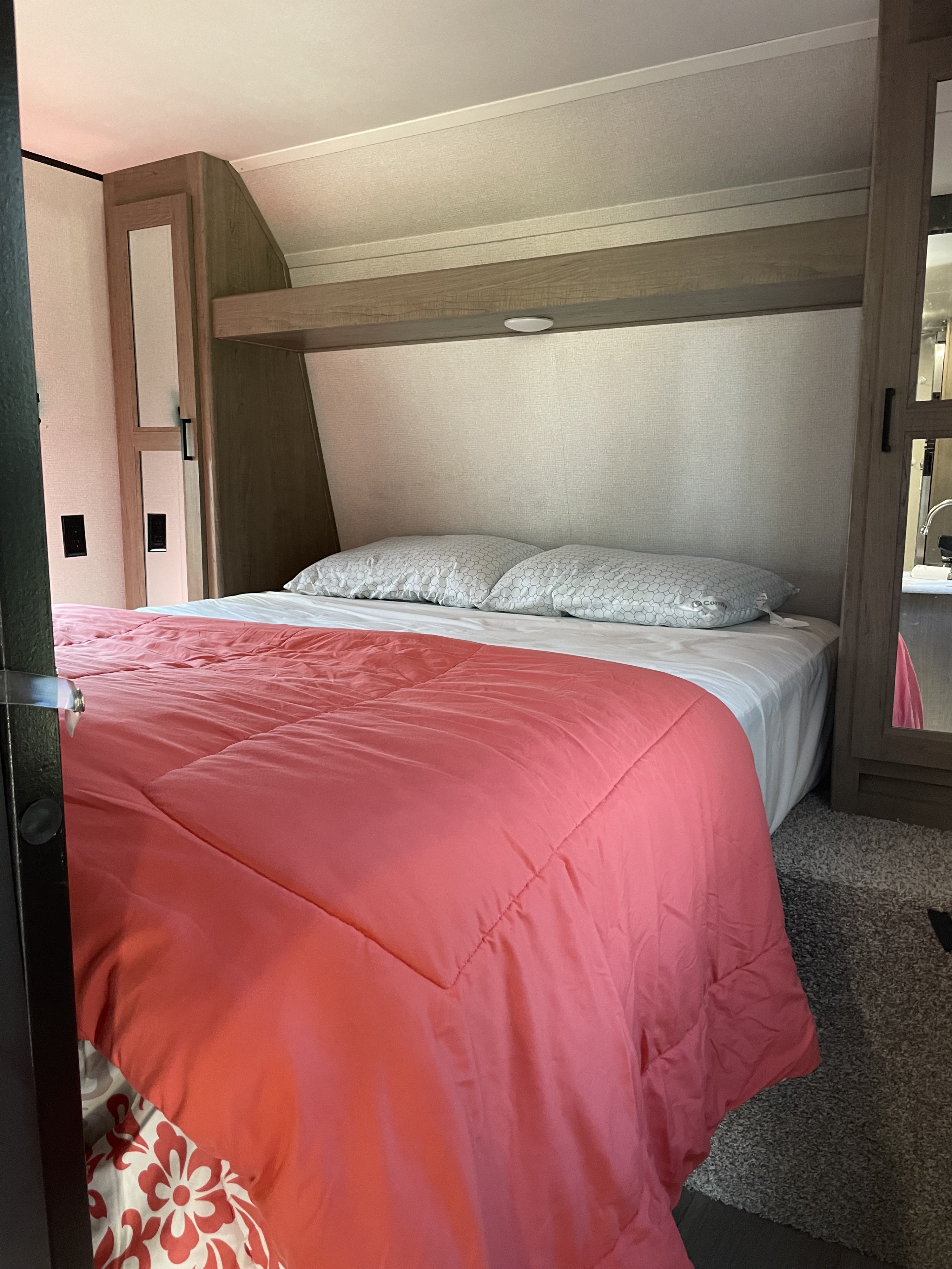 Comfortable RV rental bedroom featuring a bed with vibrant pink comforter and built-in storage.. Keystone RV Hideout 2021