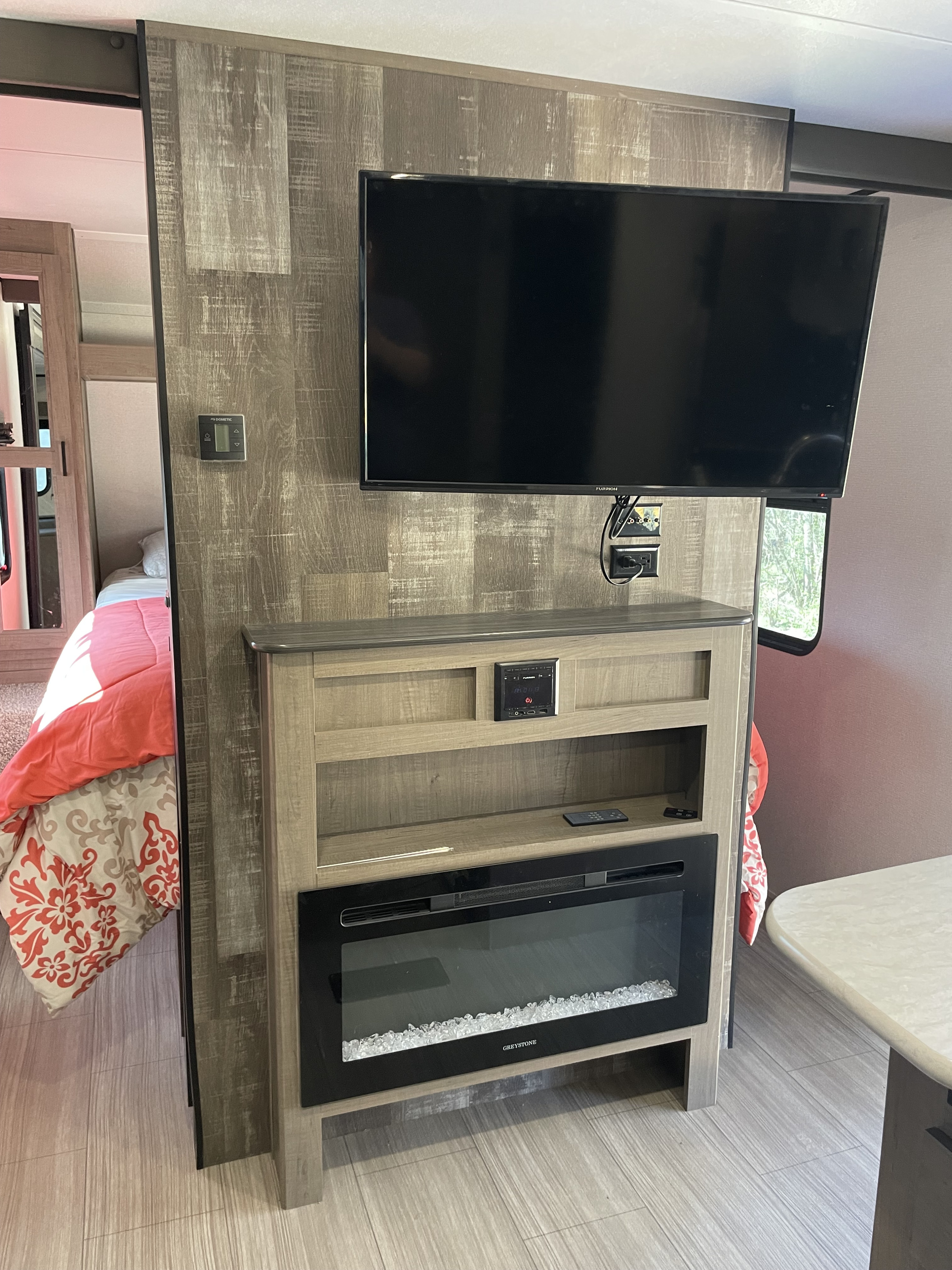 Explore this RV rental's modern interior: a TV, electric fireplace, and a cozy bedroom space with patterned bedding.. Keystone RV Hideout 2021