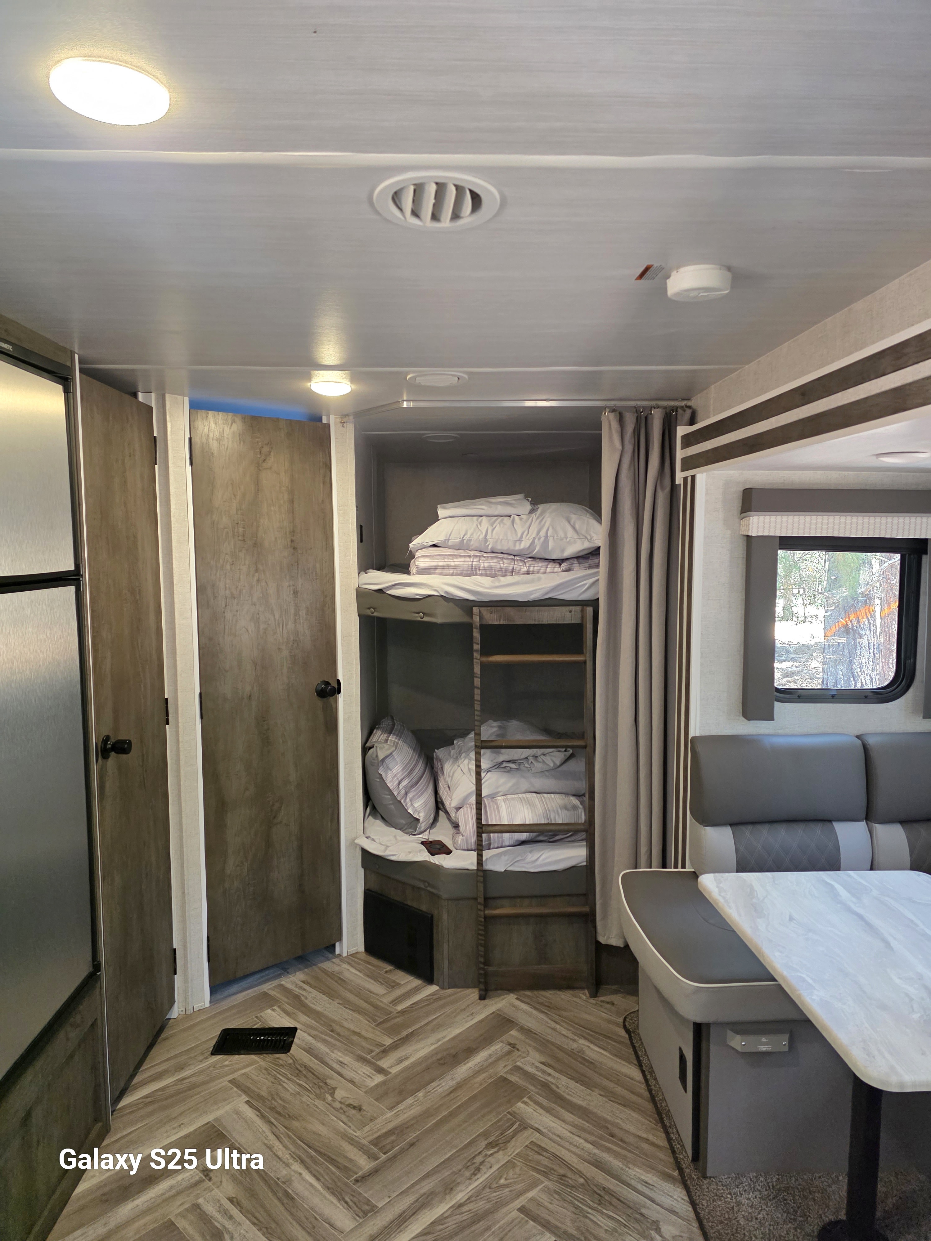 Inside a compact RV rental, featuring stacked bunk beds, a dining booth, and a small kitchen area. Ideal for mobile living.. Forest River Wildwood 2021
