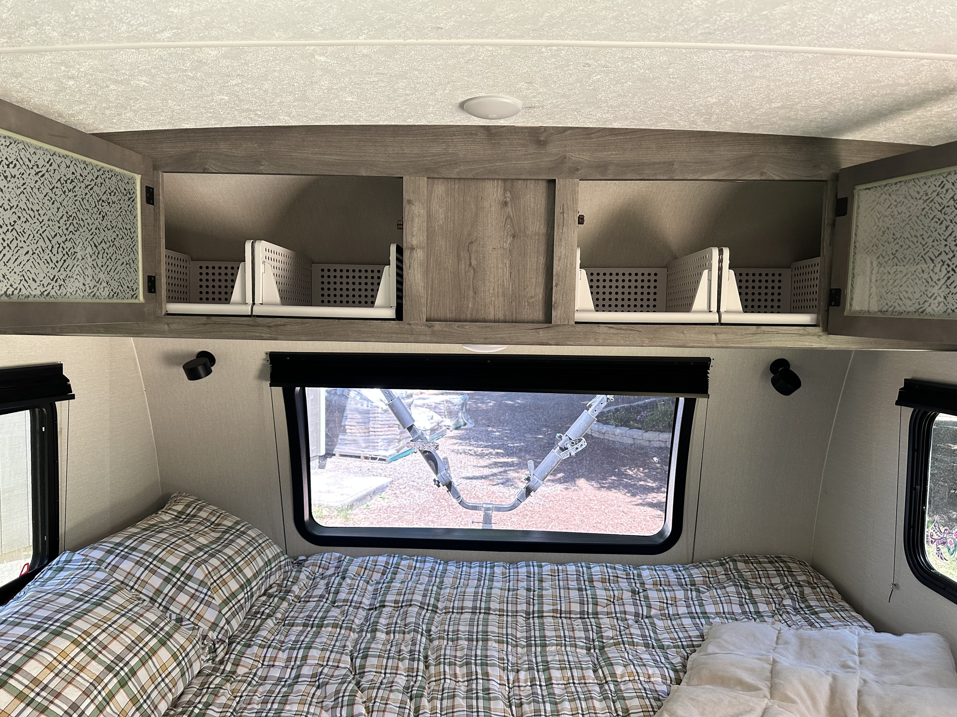 RV rental bedroom: cozy bed with plaid bedding, overhead cabinets showing storage baskets, and a window view.. Coachmen Apex Nano 2021