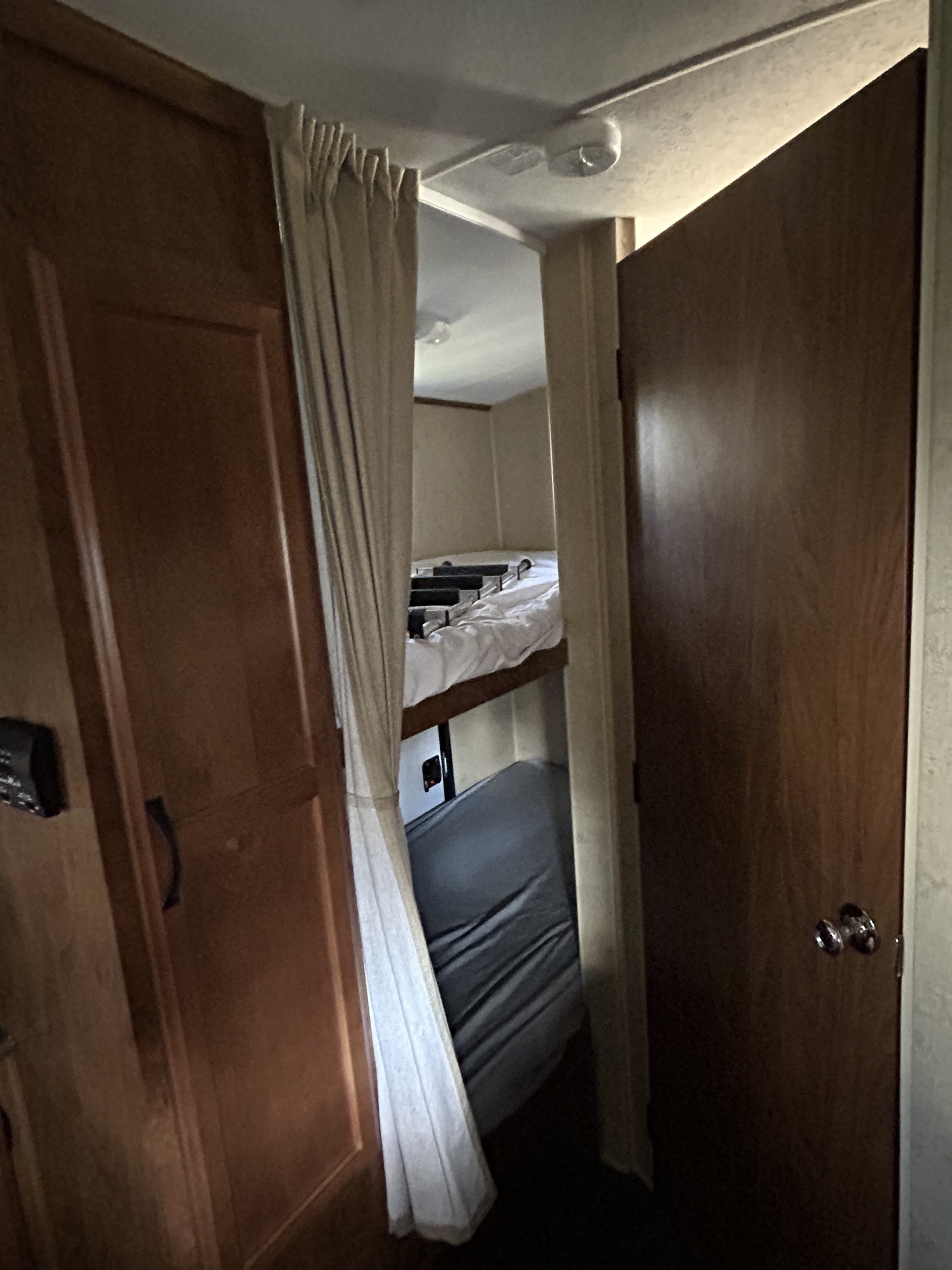 RV rental interior showing a compact bunk bed area (top bed with white bedding, lower with gray mattress), a cabinet, and a door.. Outdoors RV 22BHS 2019