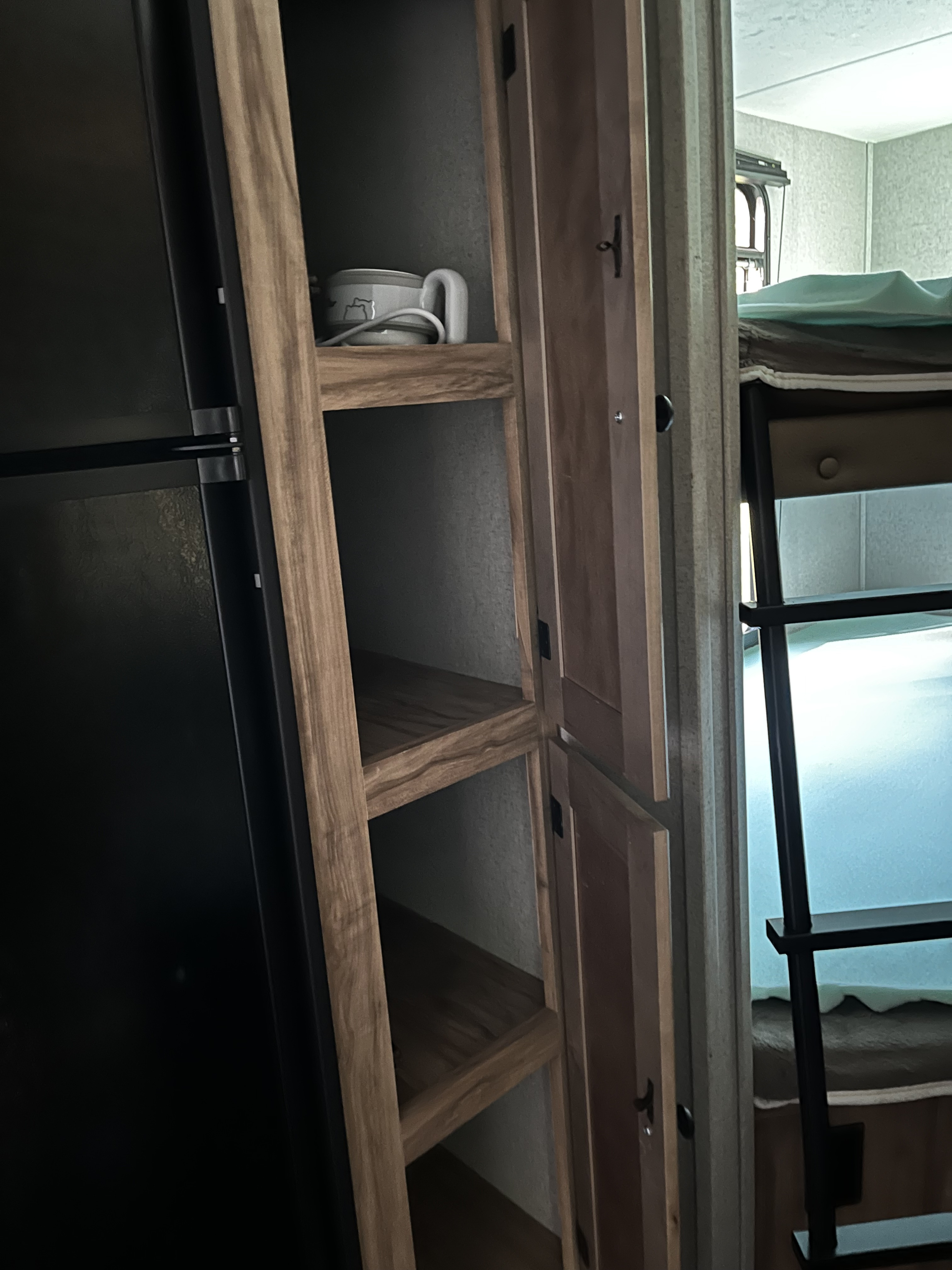 RV rental interior showing a black fridge, open shelves with a mug, and a bunk bed ladder.. Forest River Coachmen Freedom Express Ultra Lite 2019