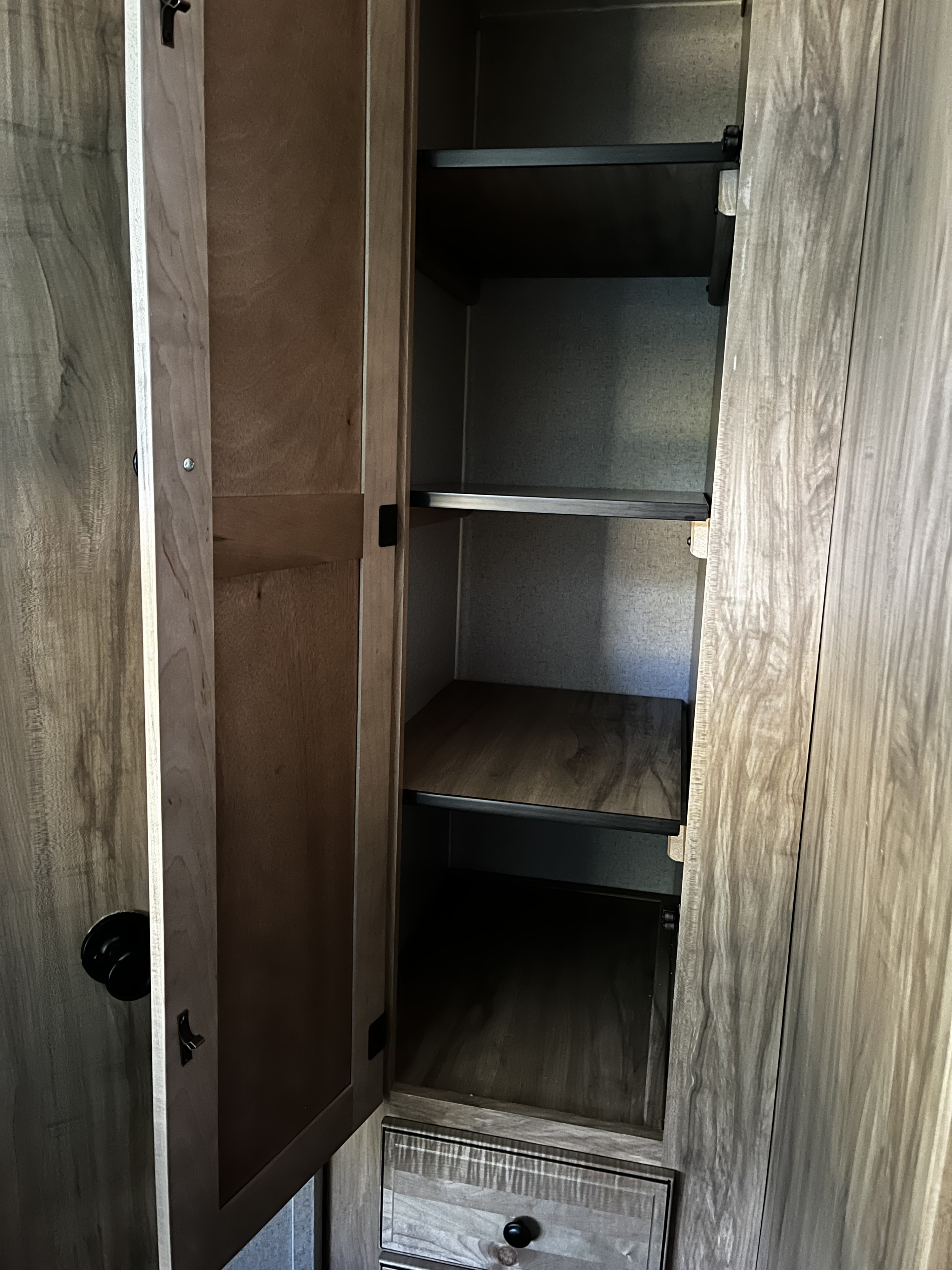 Spacious RV rental cabinet, open to reveal light wood shelves and a lower drawer, offering practical storage for your journey.. Forest River Coachmen Freedom Express Ultra Lite 2019