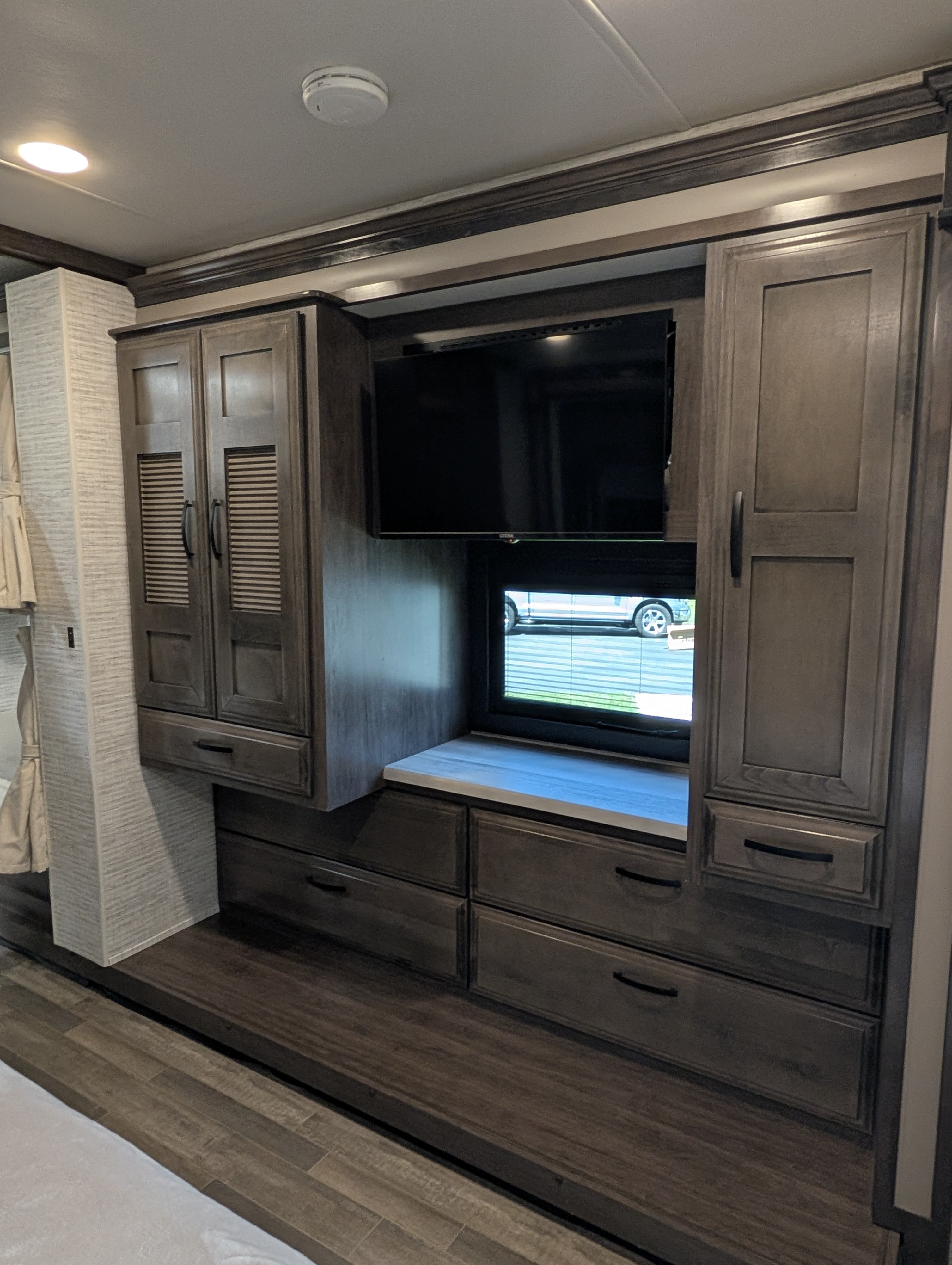 Modern RV rental interior showing a dark wood wall unit with a TV, window, and ample storage cabinets & drawers.. Jayco Precept 2025