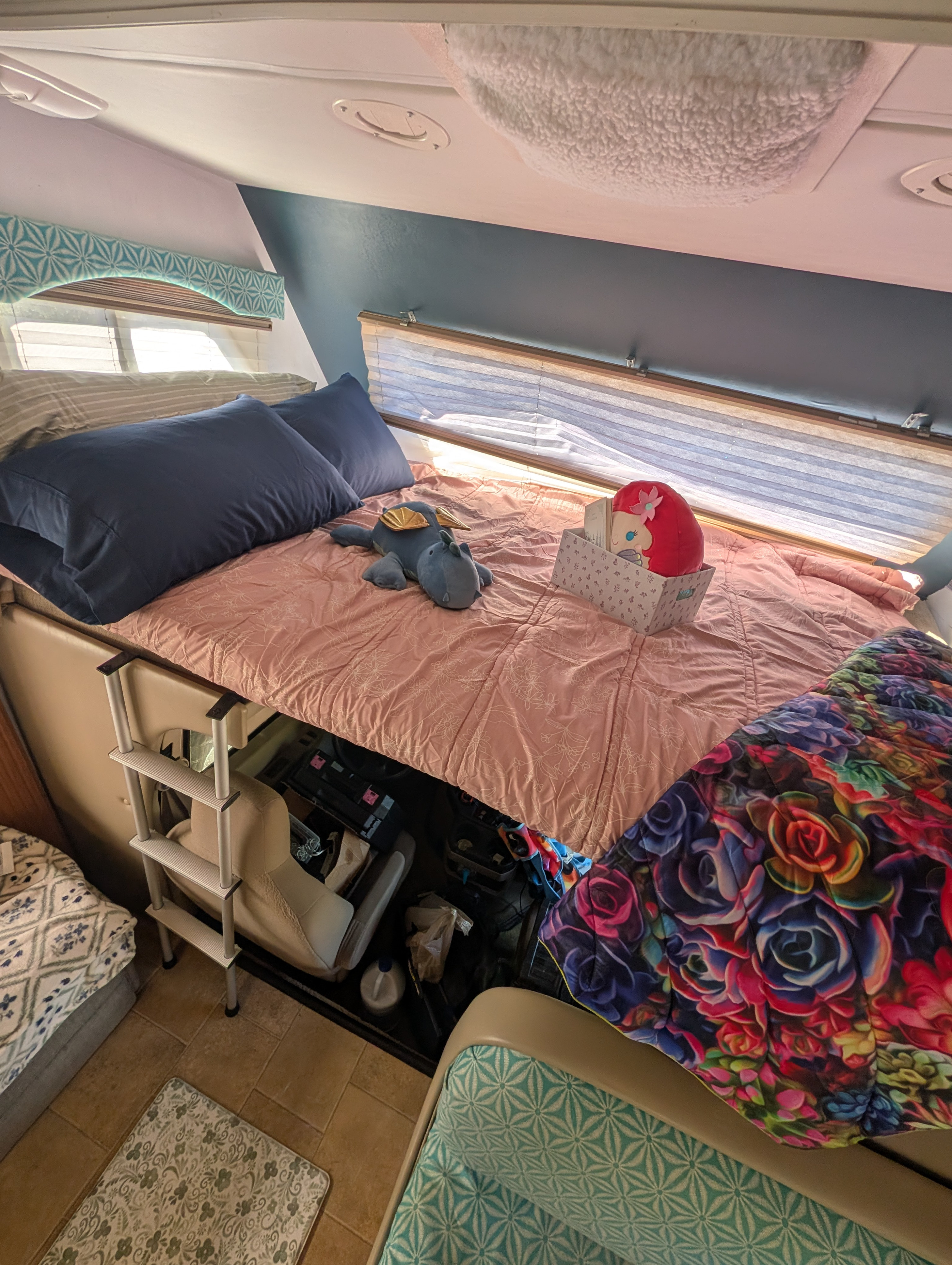 Cozy RV rental bedroom featuring a raised bed with pink bedding, blue pillows, playful decor, and access ladder.. Four Winds Freedom Elite 2011