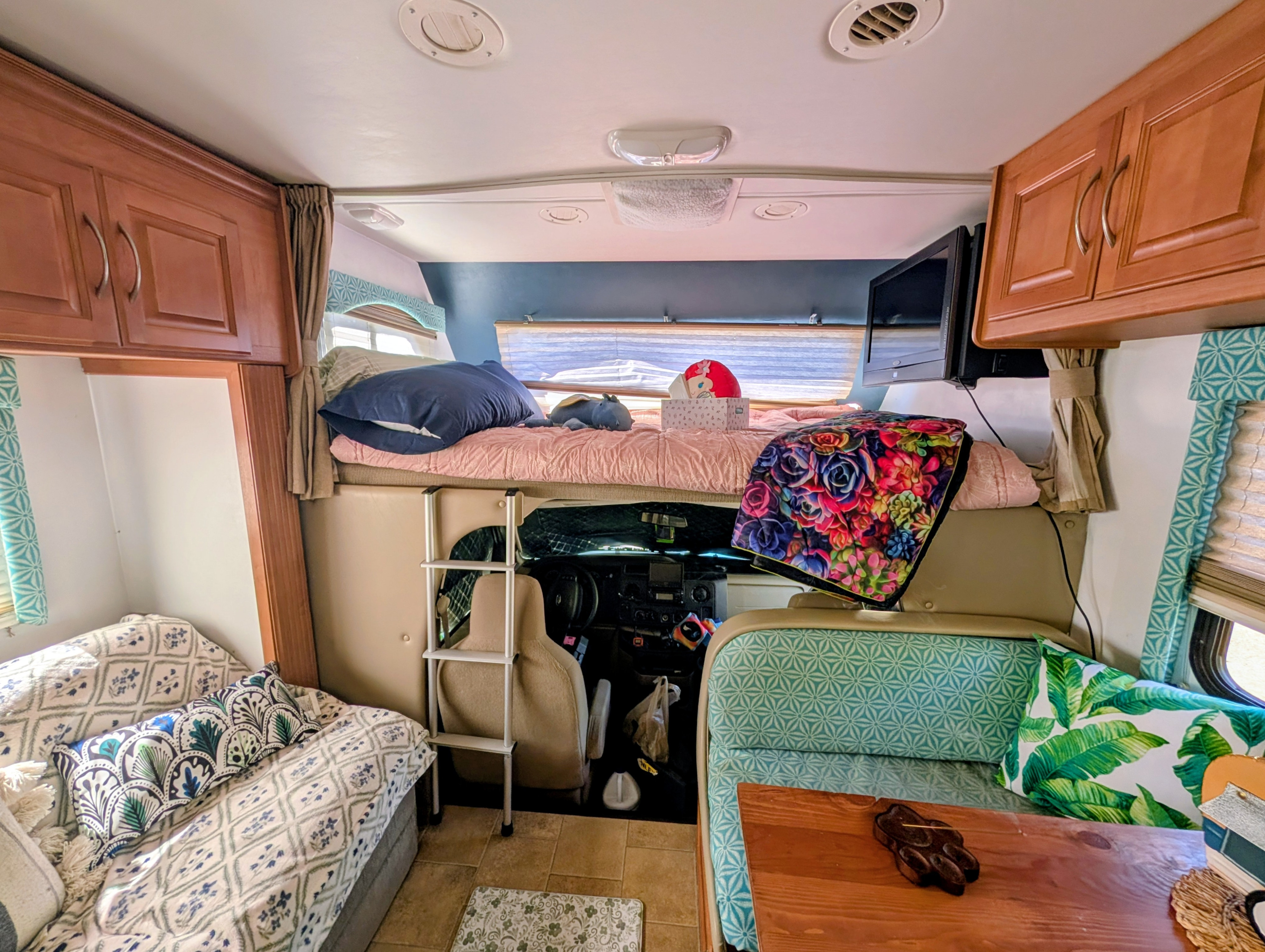 Inside an RV rental, featuring a bed over the cockpit, dinette, and sofa seating with colorful pillows.. Four Winds Freedom Elite 2011