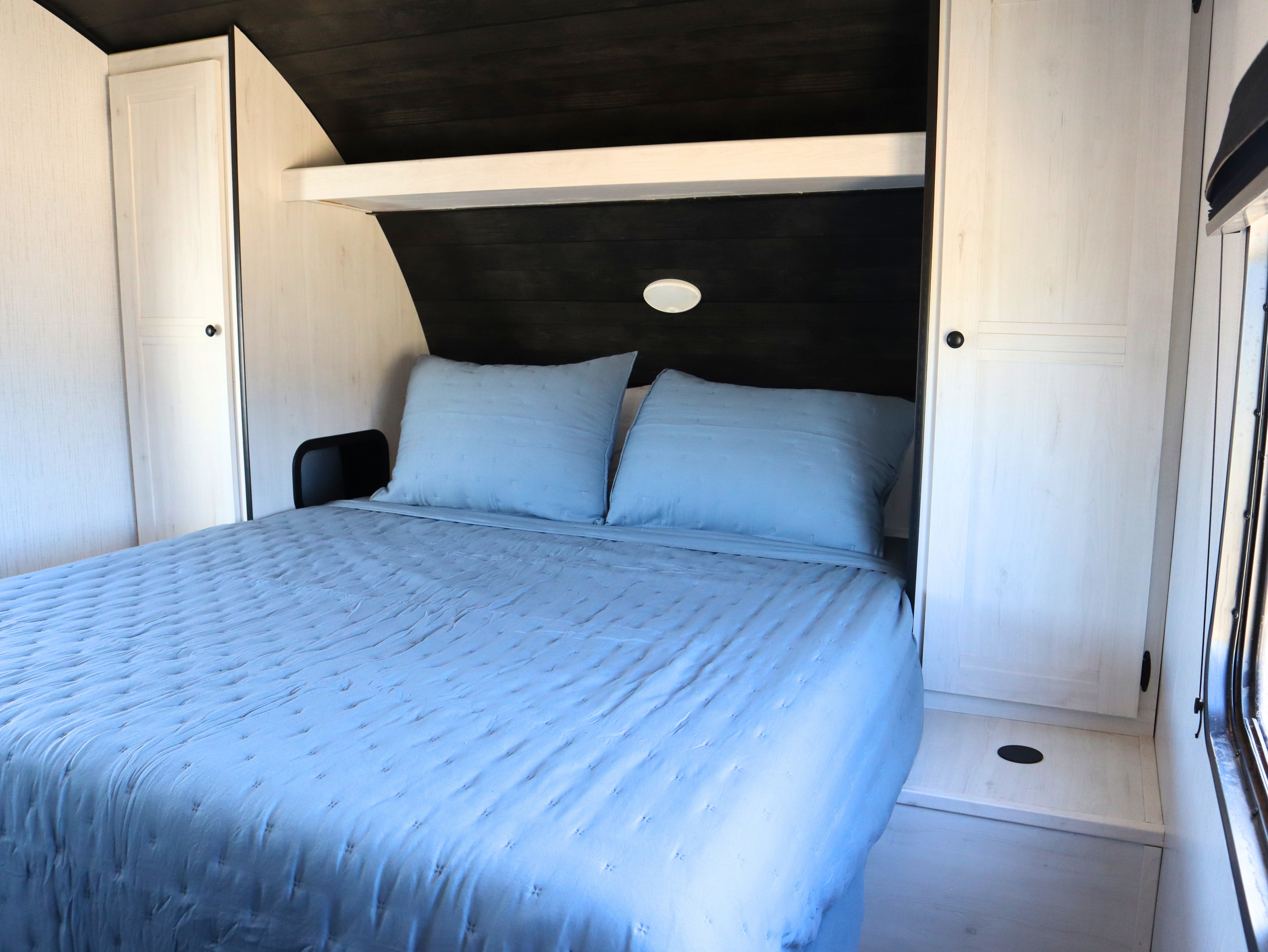 This cozy RV rental bedroom offers a comfortable bed with blue quilted bedding, built-in storage, and modern wood finishes.. Heartland RVs Trail Runner 2022