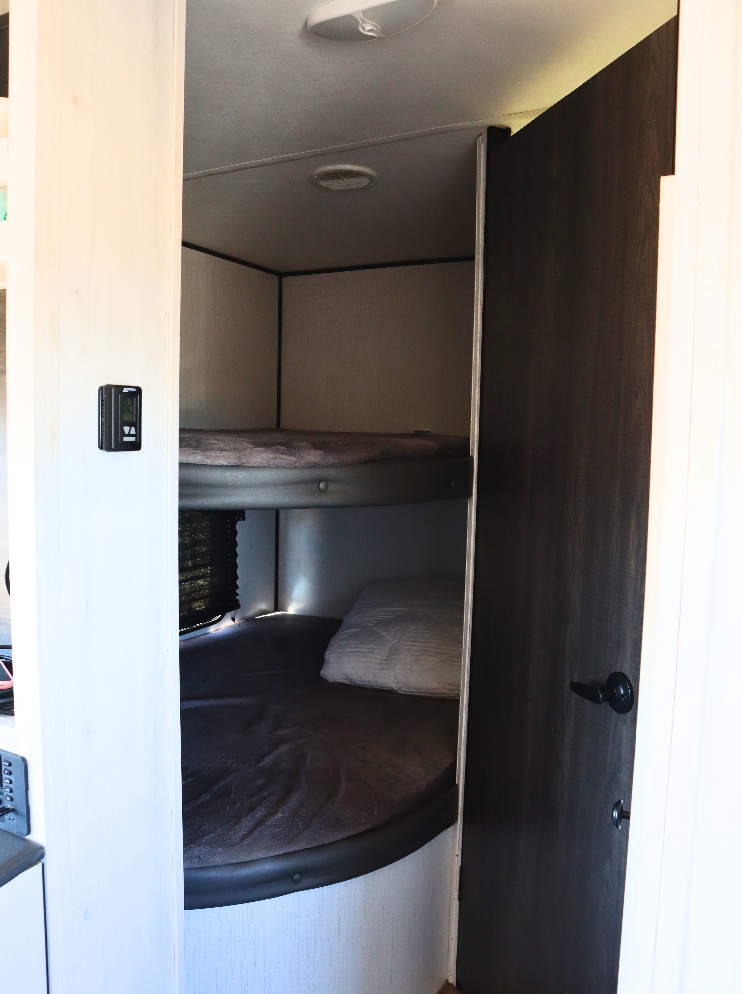 RV rental interior features two bunk beds with bedding for guests, a wall-mounted thermostat is visible on the left.. Heartland RVs Trail Runner 2022