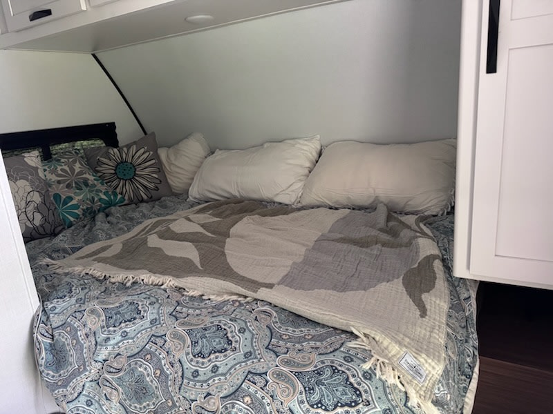 Relax in this cozy RV rental bedroom. Features a comfortable bed with patterned bedding, pillows, and overhead storage.. Keystone Passport 190RDWE 2026