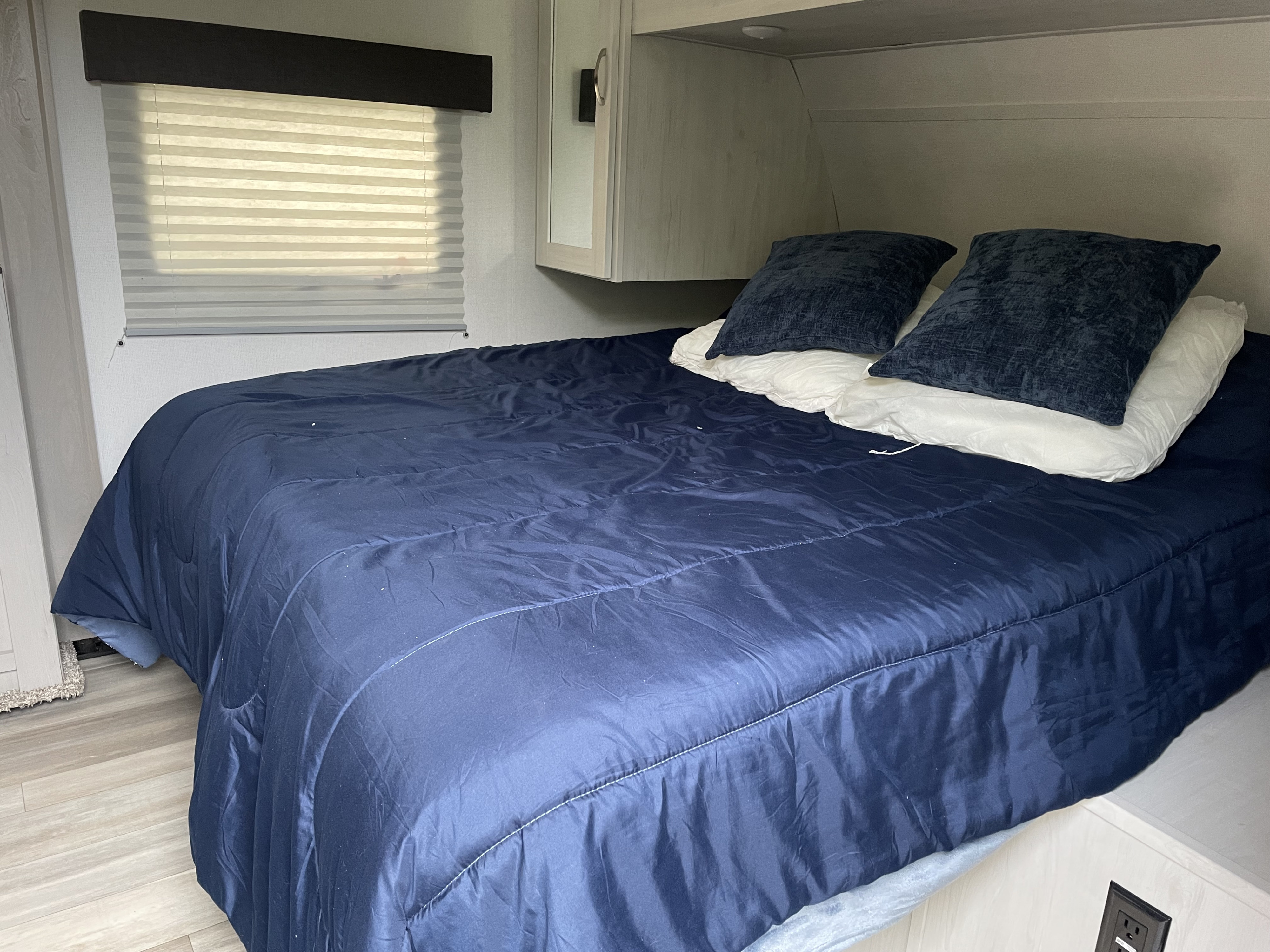 Cozy RV rental bedroom with a large bed, dark blue comforter, pillows, window blinds, and light-toned walls for comfort.. Forest River Tracer LE 2022