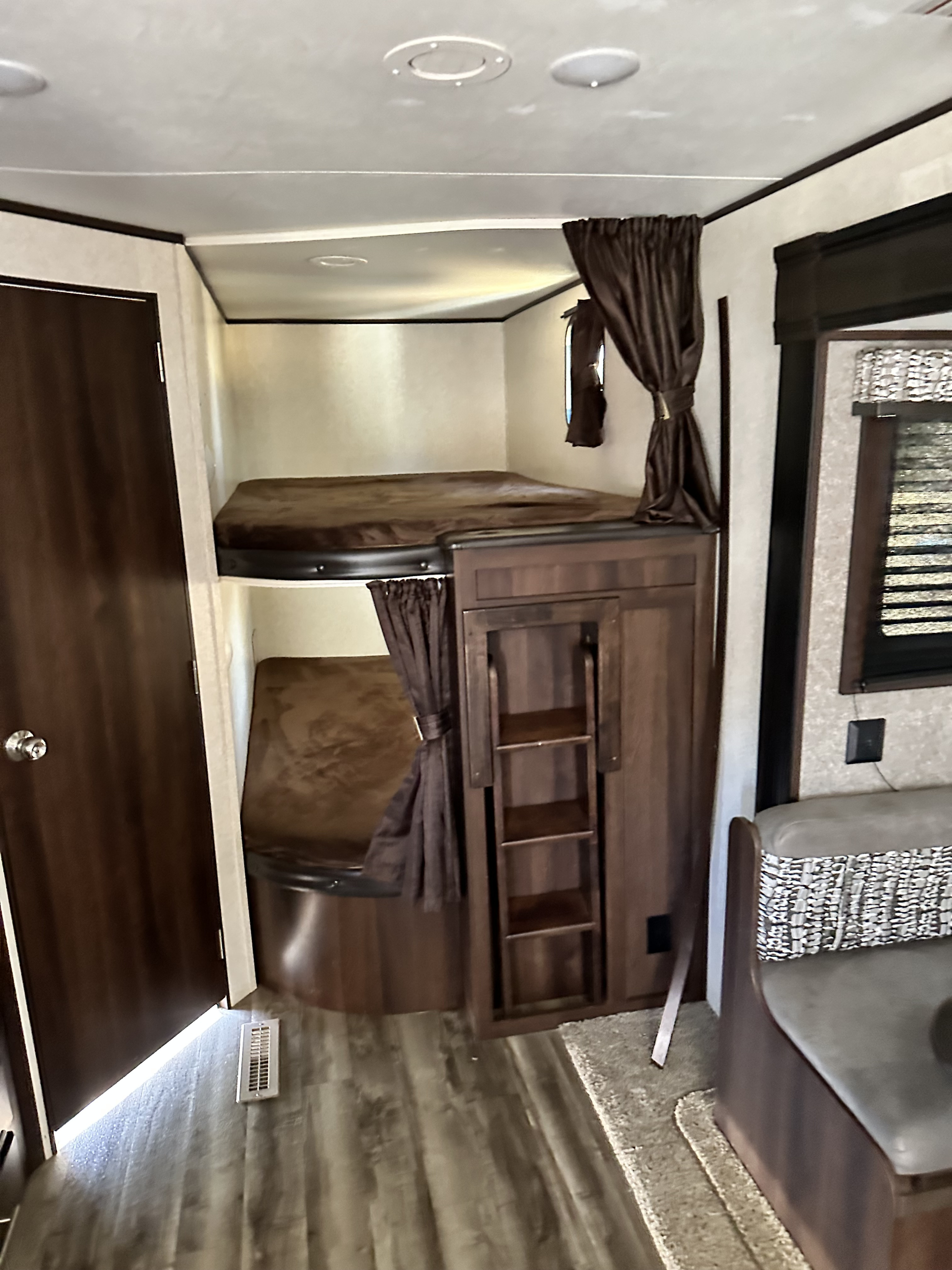 Inside an RV rental: upper and lower bunk beds with a ladder, a cozy dining bench, and dark wood finishes.. Jayco Jay Flight 2020