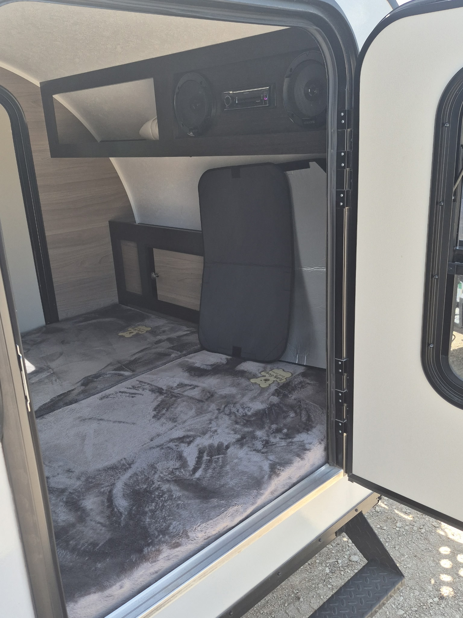 Interior view of an **rv rental** showing a gray bed, overhead storage with speakers, and a stereo unit. Steps lead outside.. BUSHWACKER 10HD 2024