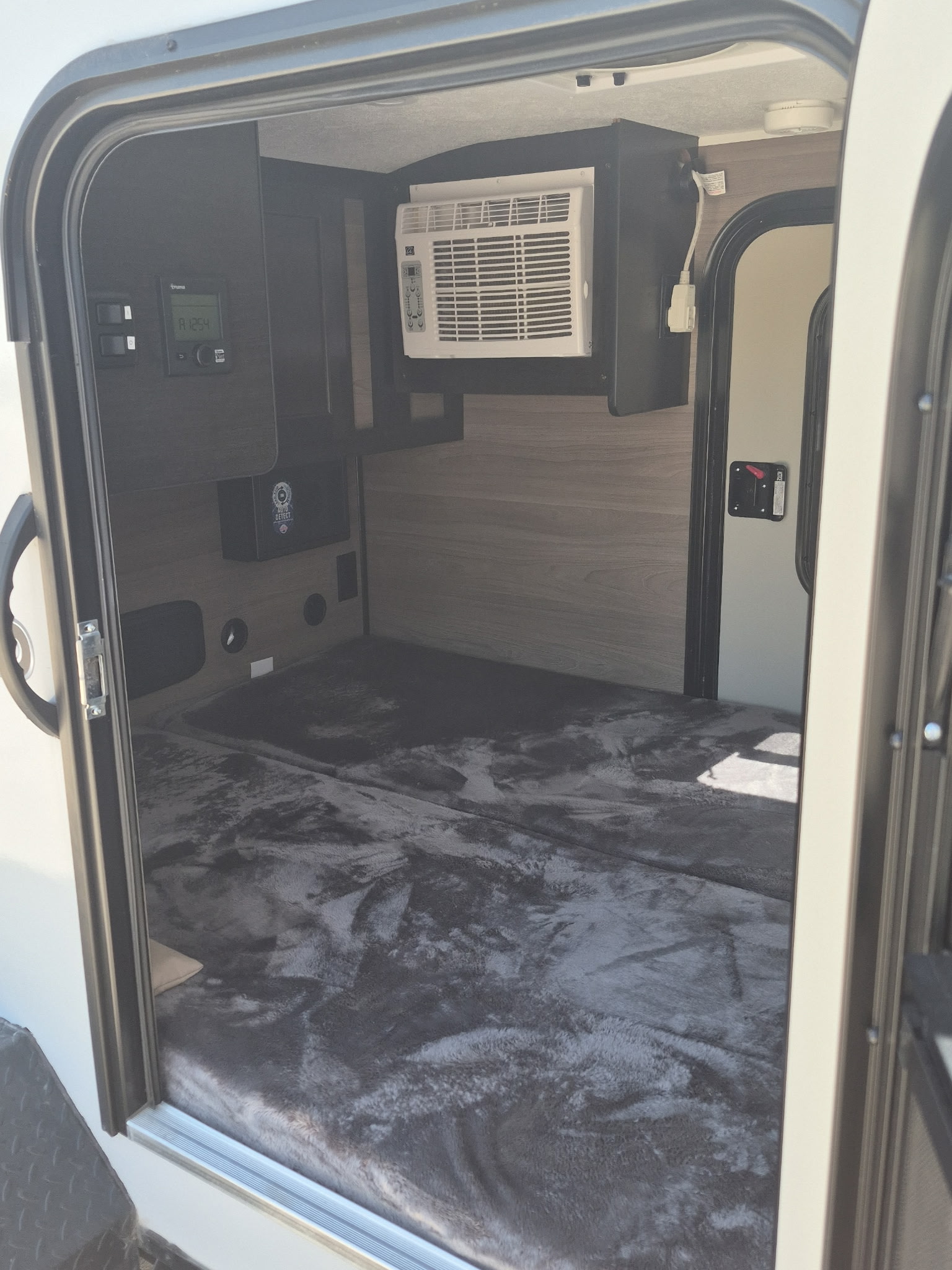 Compact RV rental interior featuring a comfy bed, mounted AC unit, and control panel on the left.. BUSHWACKER 10HD 2024