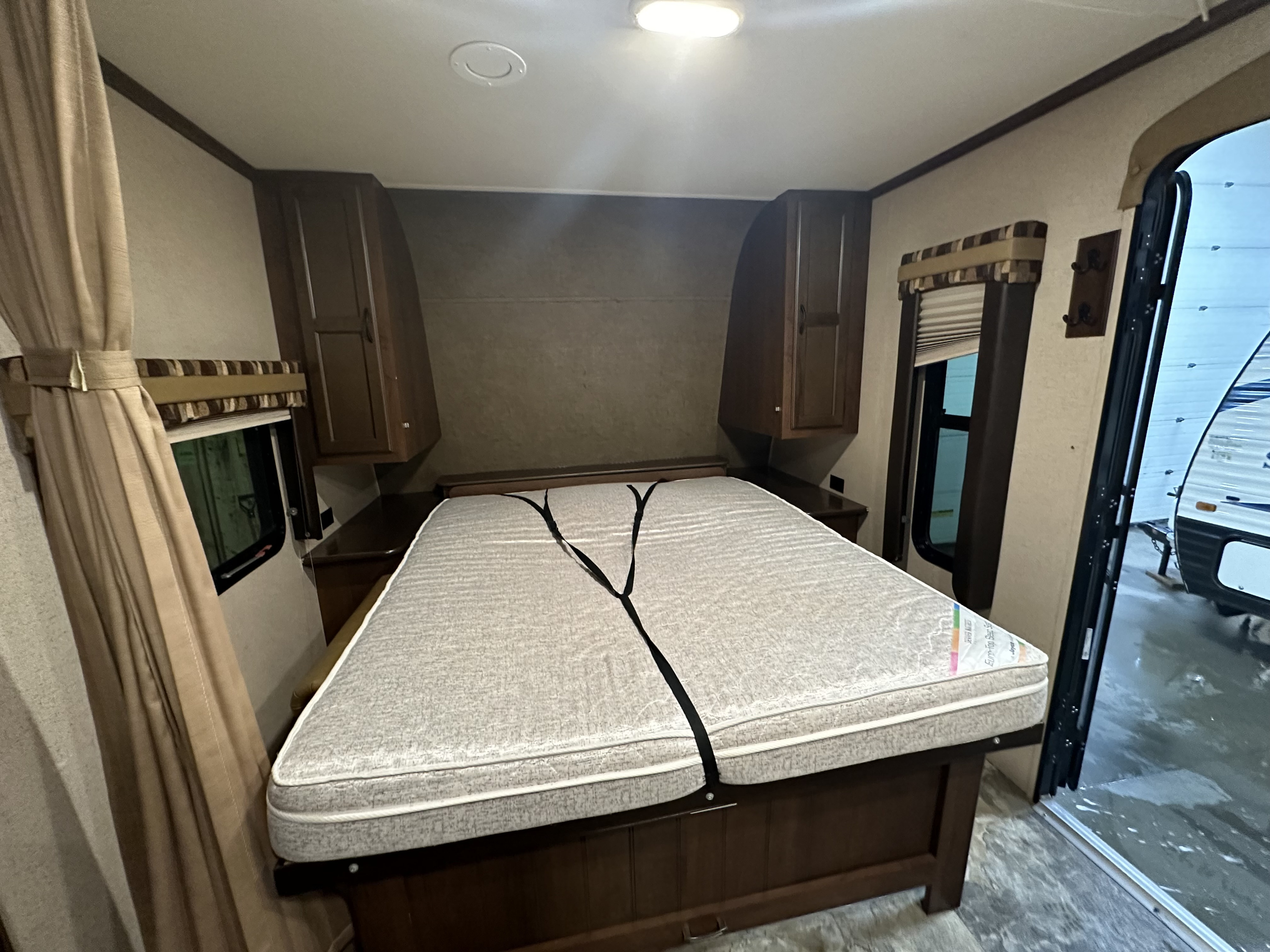RV rental bedroom featuring a secured bed, wooden cabinets, windows, and an open door showing another RV outside.. Jayco Jay Flight 2015