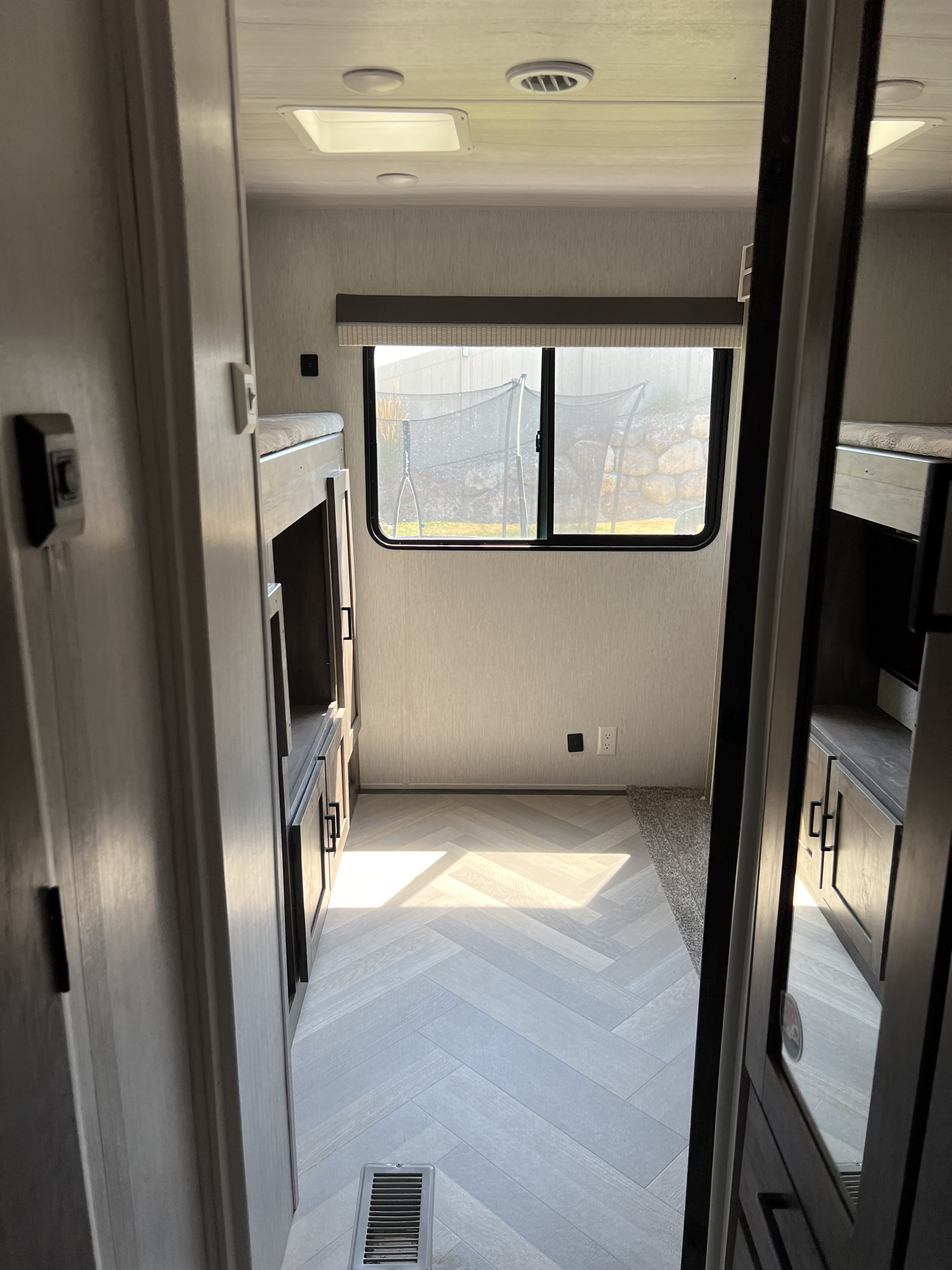 Spacious RV rental bunkhouse with light wood-look herringbone floors, built-in bunk beds, storage, & a bright window.. Forest River Wildwood 2022