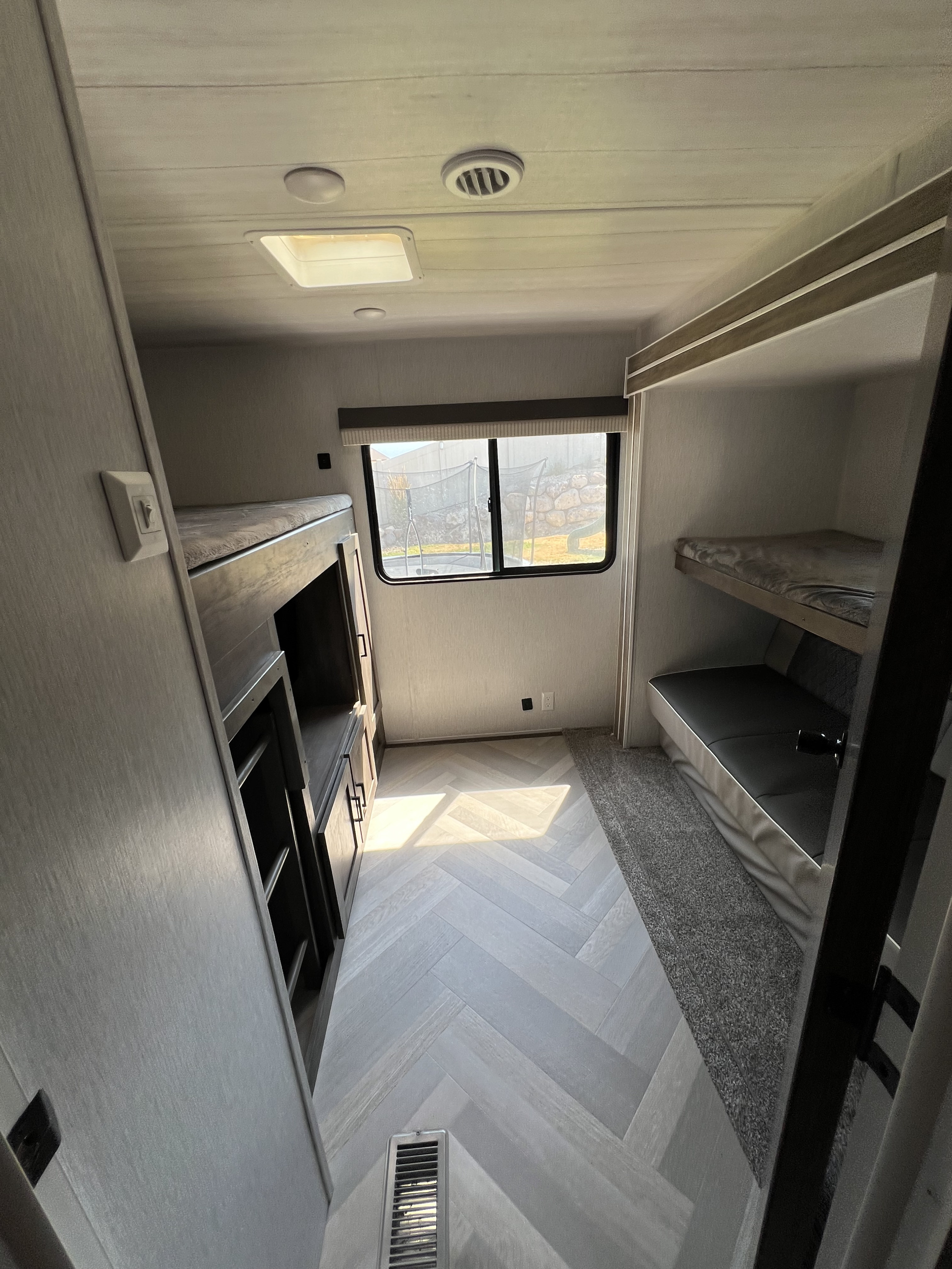 Modern rv rental bunkhouse with light herringbone floor, a window view, and multiple bunk beds in a bright interior.. Forest River Wildwood 2022