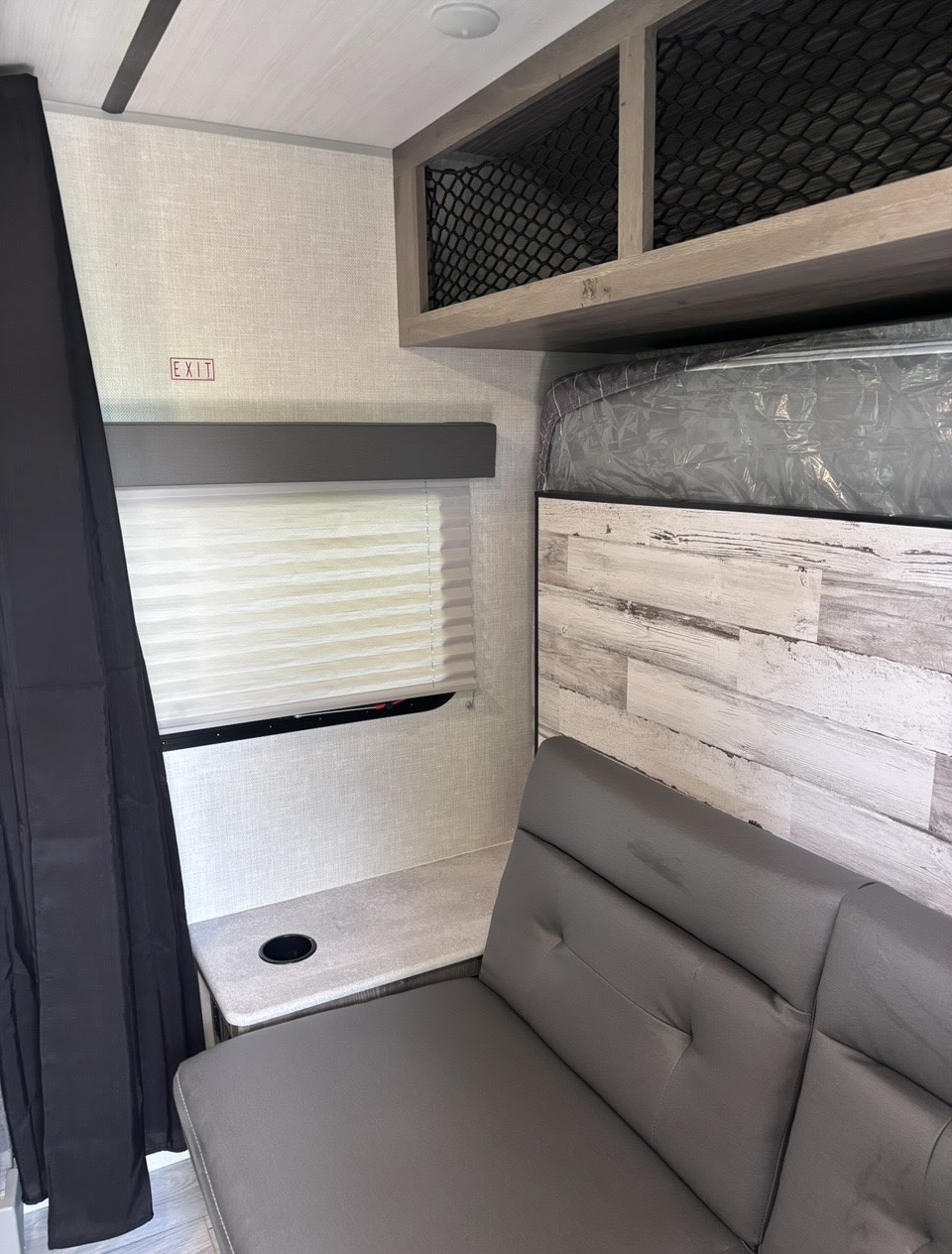 RV rental interior: featuring a bunk bed, grey sofa seating, a window with blinds, and overhead net storage. Exit clearly marked.. Forest River Surveyor Legend 2022