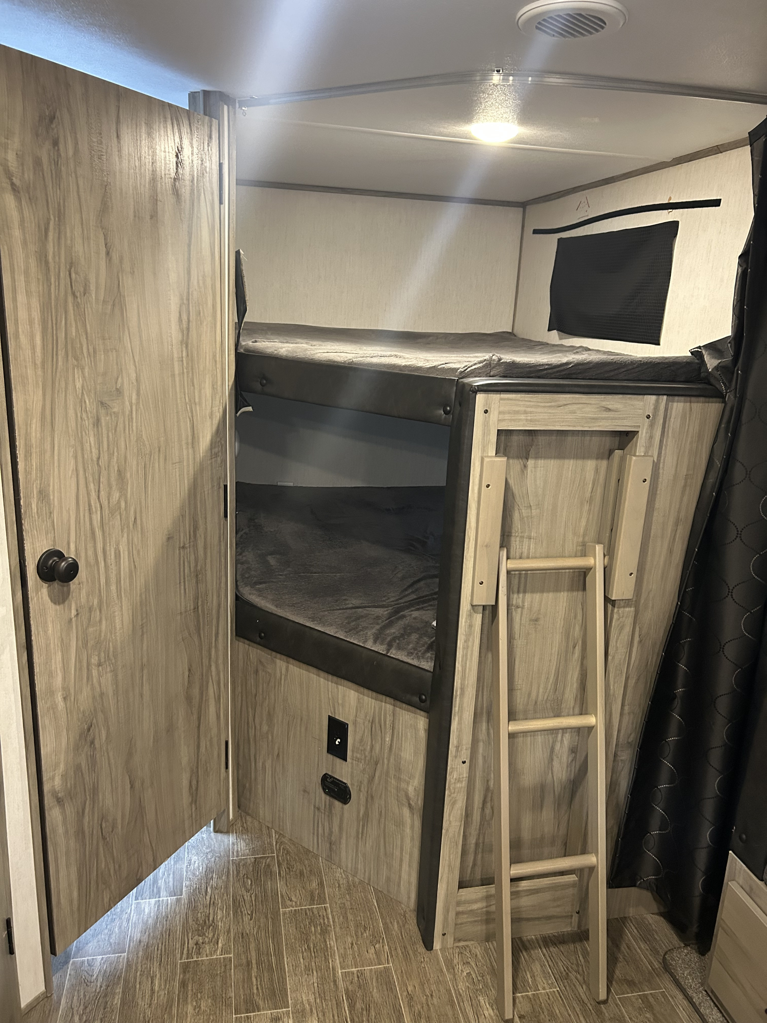 A cozy bunk bed sleeping area with a ladder inside an rv rental, featuring wood-look finishes and dark bedding.. Forest River Cherokee Alpha Wolf 2021