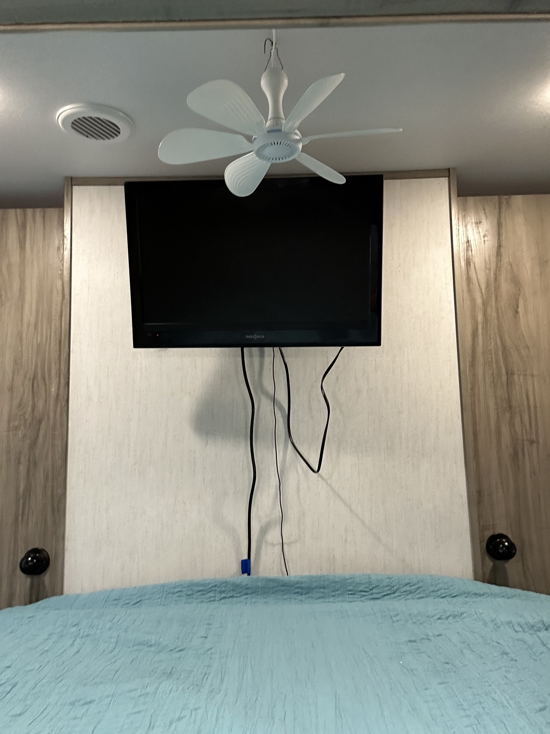 RV rental bedroom: Mounted TV with visible wires, a small ceiling fan, and a blue bed. Compact and comfortable space.. Forest River Cherokee Alpha Wolf 2021