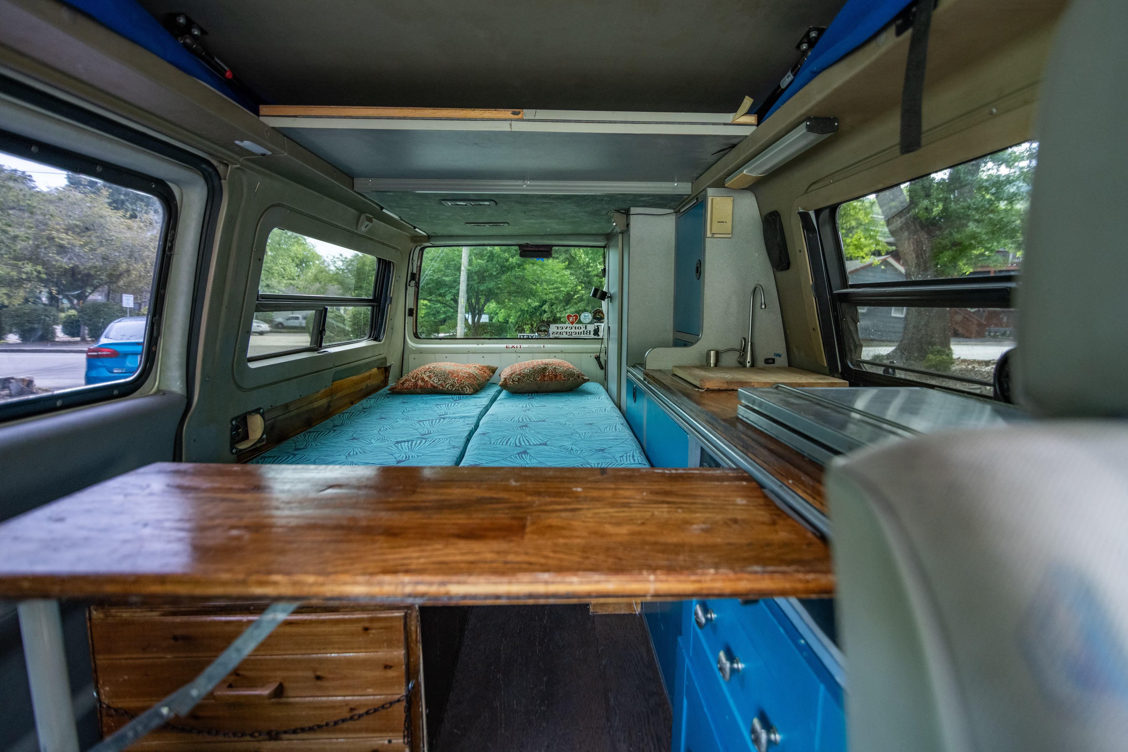 Explore this spacious camper van RV rental interior! Features include a comfy bed, functional kitchen, and wooden table.. Winnebago Eurovan Camper Eurovan Camper 1997