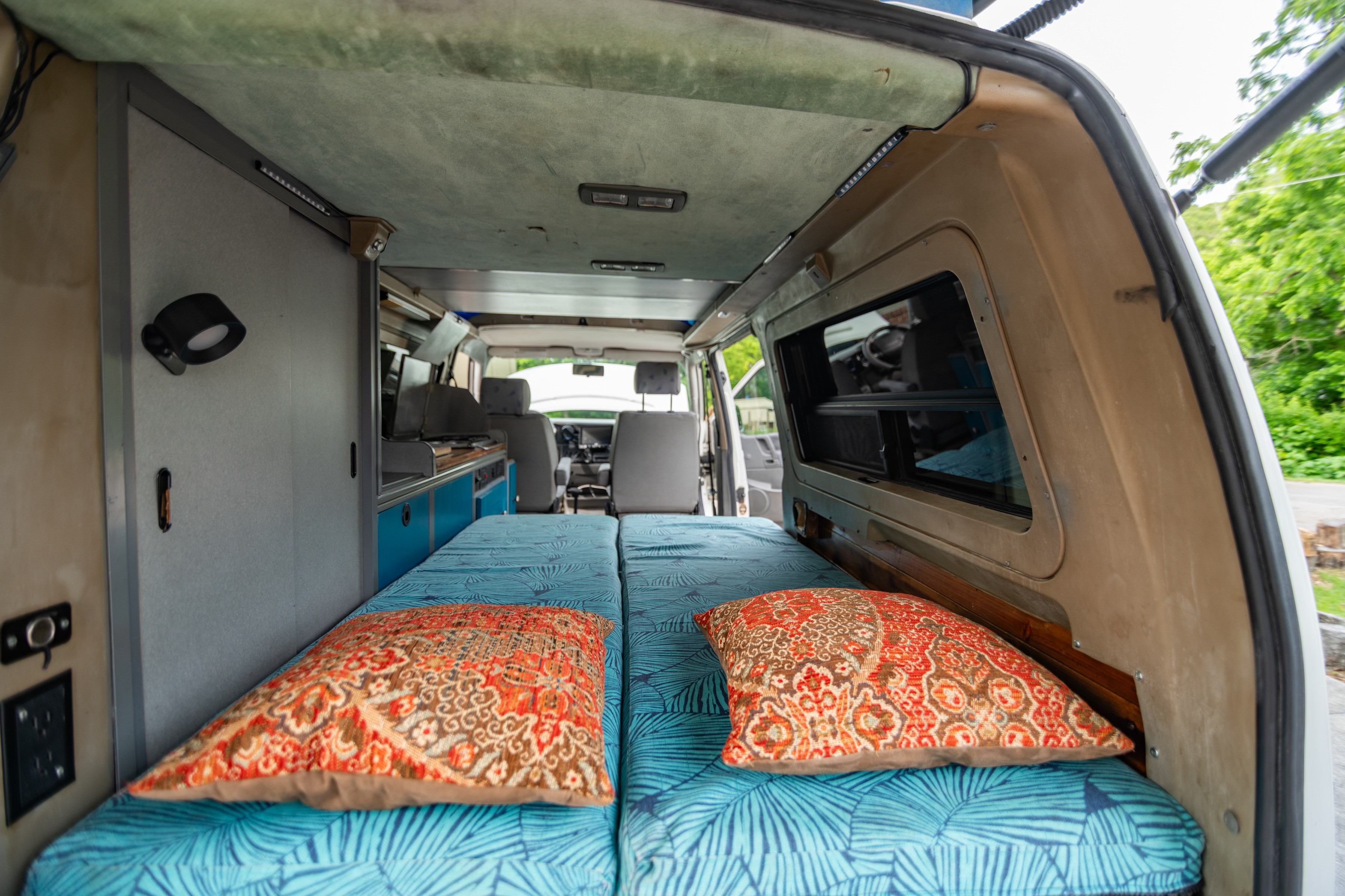 Inside a cozy RV rental camper van: comfortable beds with blue and orange cushions, facing the front seats and kitchen area.. Winnebago Eurovan Camper Eurovan Camper 1997