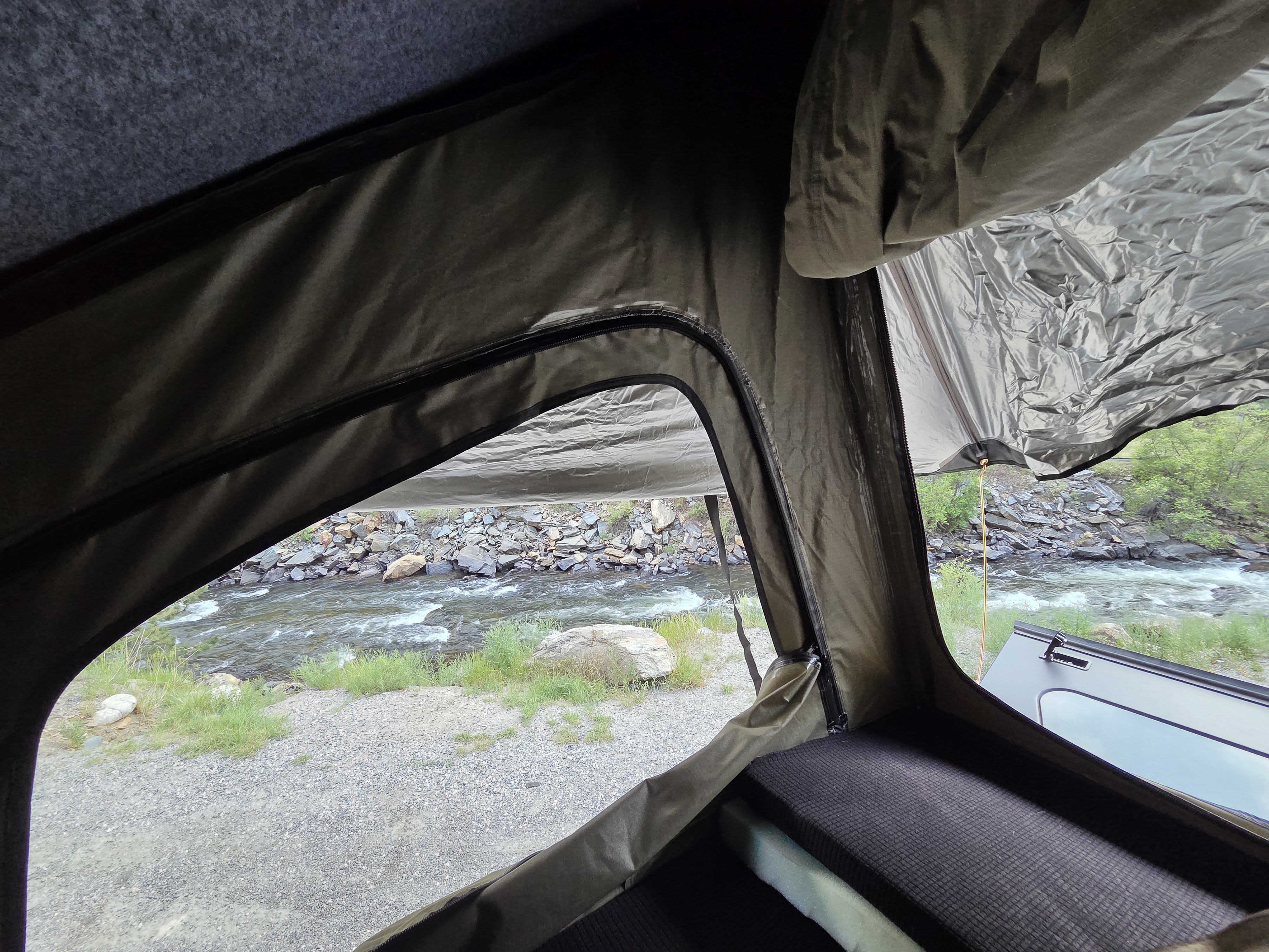 Inside an RV rental rooftop tent, a comfy sleeping area overlooks a scenic river view. Perfect for outdoor adventure.. jeep Gladiator 2021