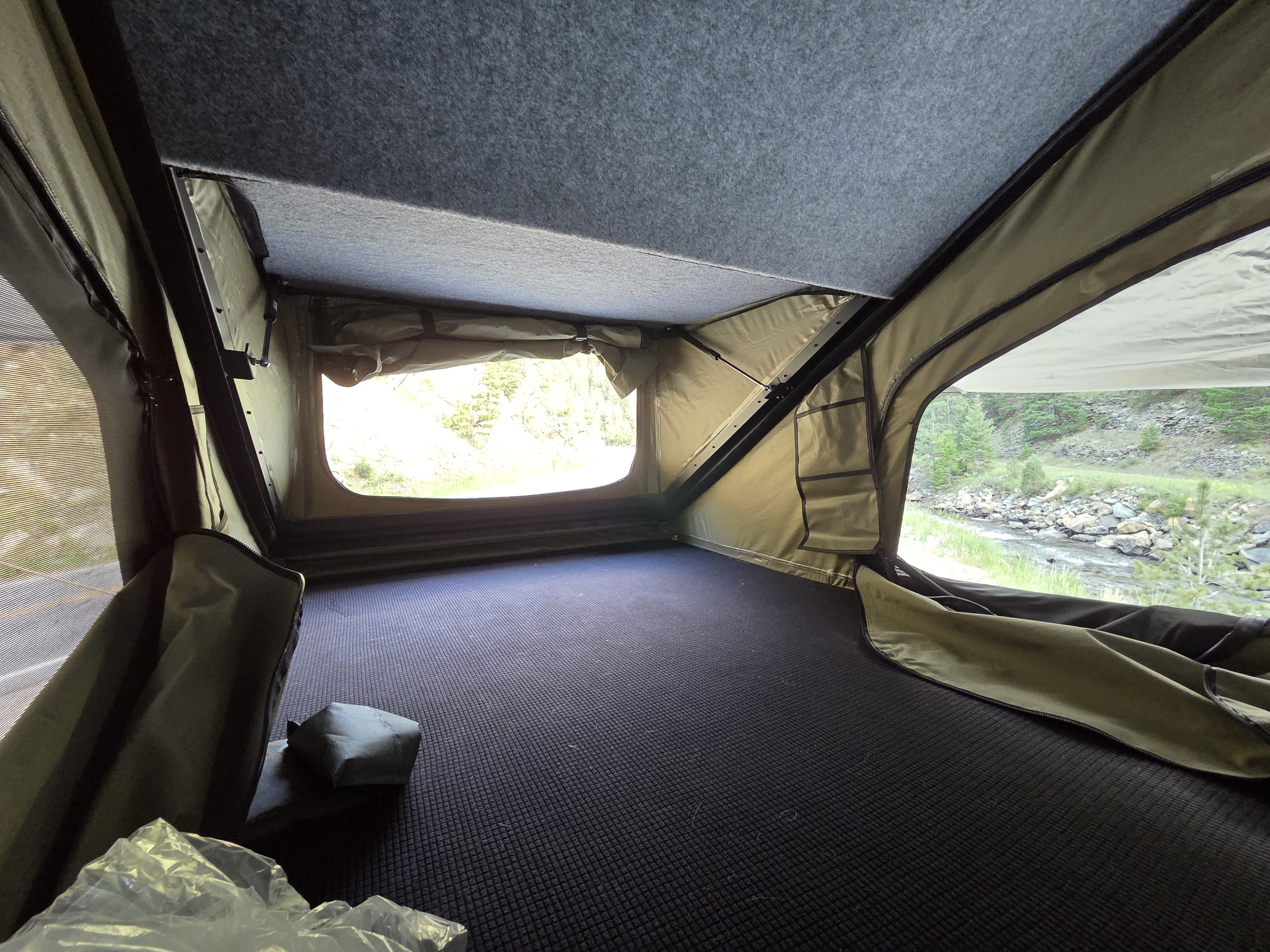 Inside a comfy rv rental rooftop tent, offering scenic river views. Features dark patterned floor, olive walls, and a grey felt ceiling.. jeep Gladiator 2021