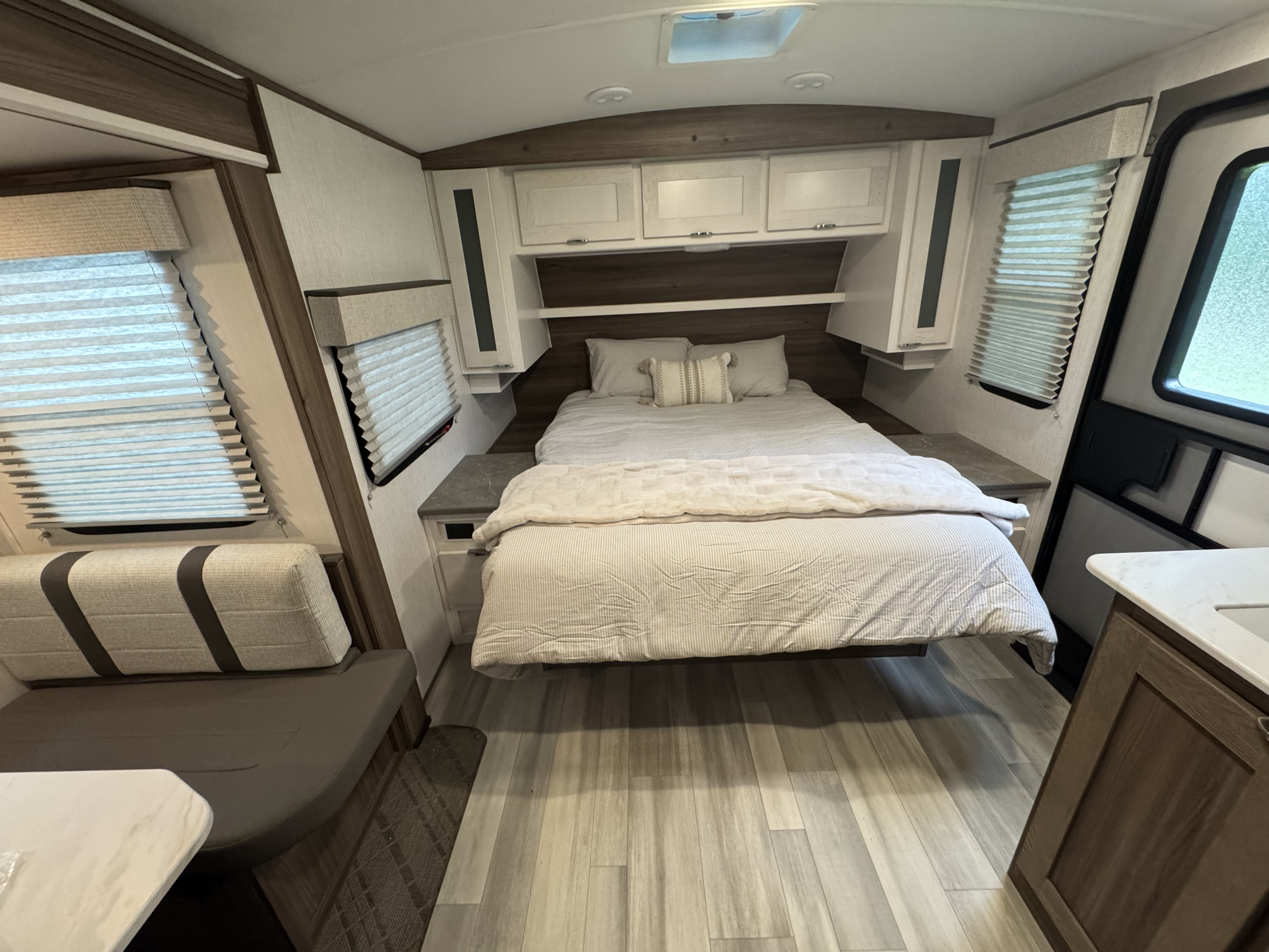 RV rental bedroom with a full bed, overhead cabinets, light wood flooring, and a cozy dinette. Modern, bright interior.. Cruiser RV MPG 2023