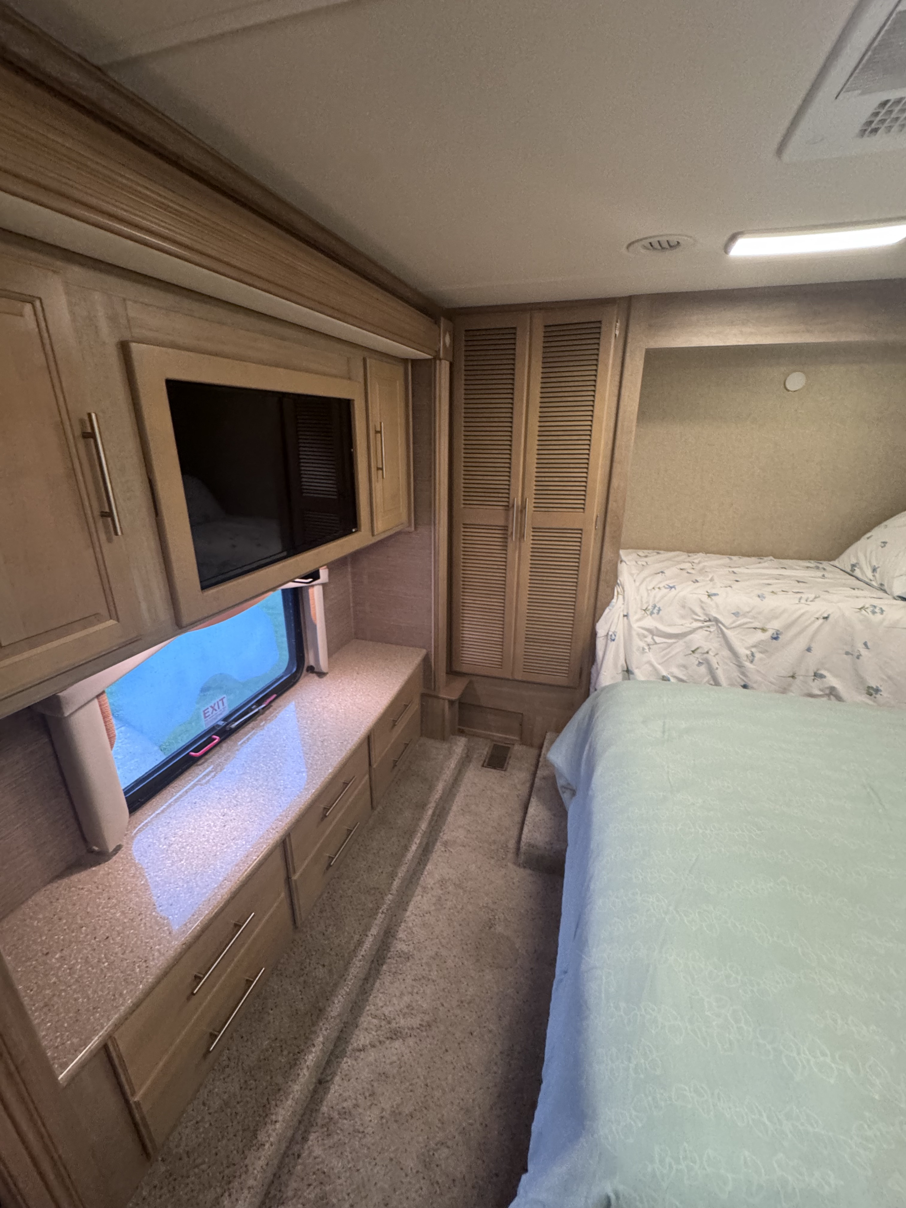 Inside an RV rental: a comfortable bedroom with two beds, wood cabinetry, TV, and a window, ideal for your next trip.. Forest River Coachmen Pathfinder 2014