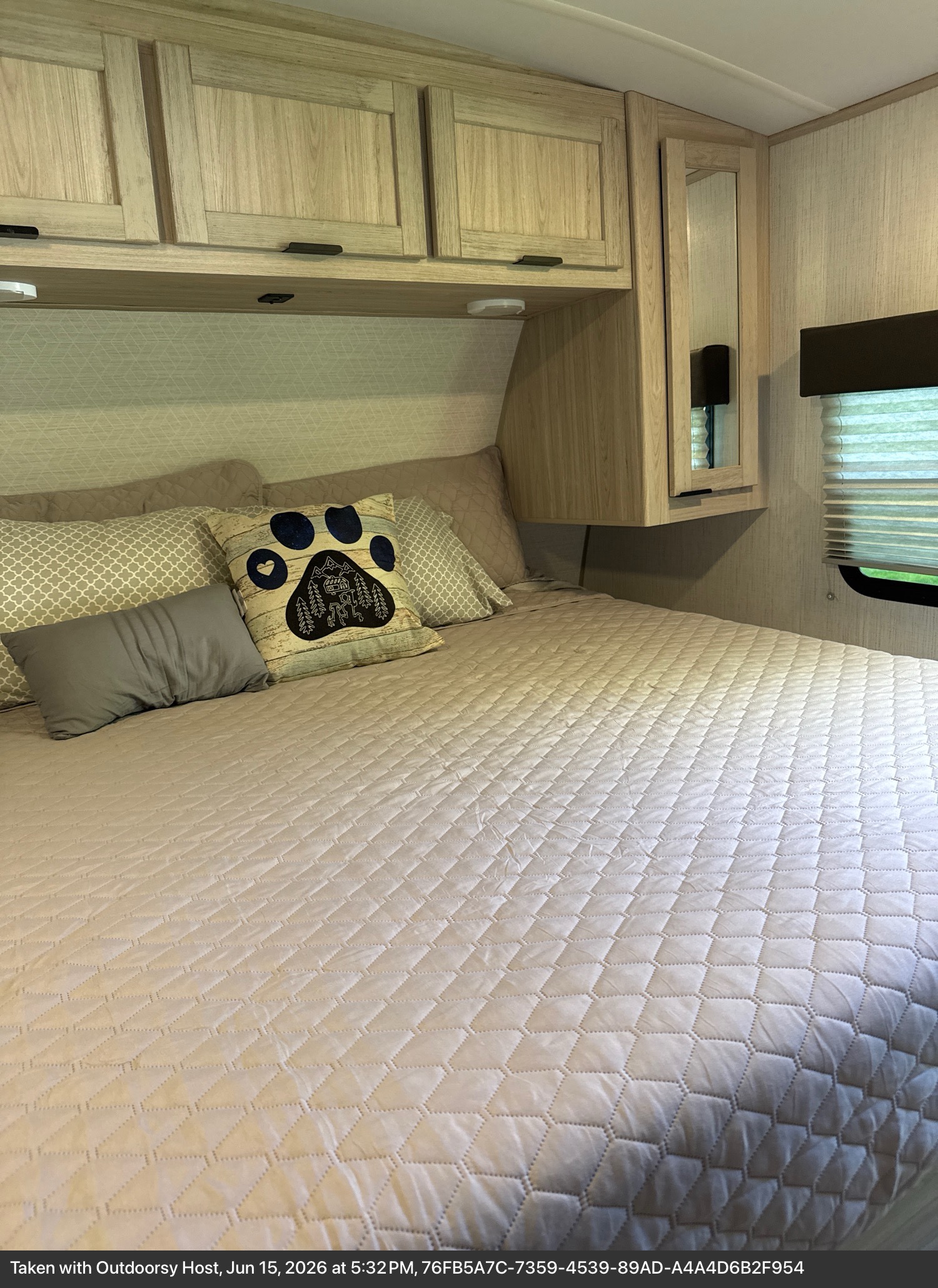 Cozy RV rental bedroom with quilted bed, paw print pillow, overhead cabinets, mirror, and window with blinds.. Cruiser RV Shadow Cruiser 2022