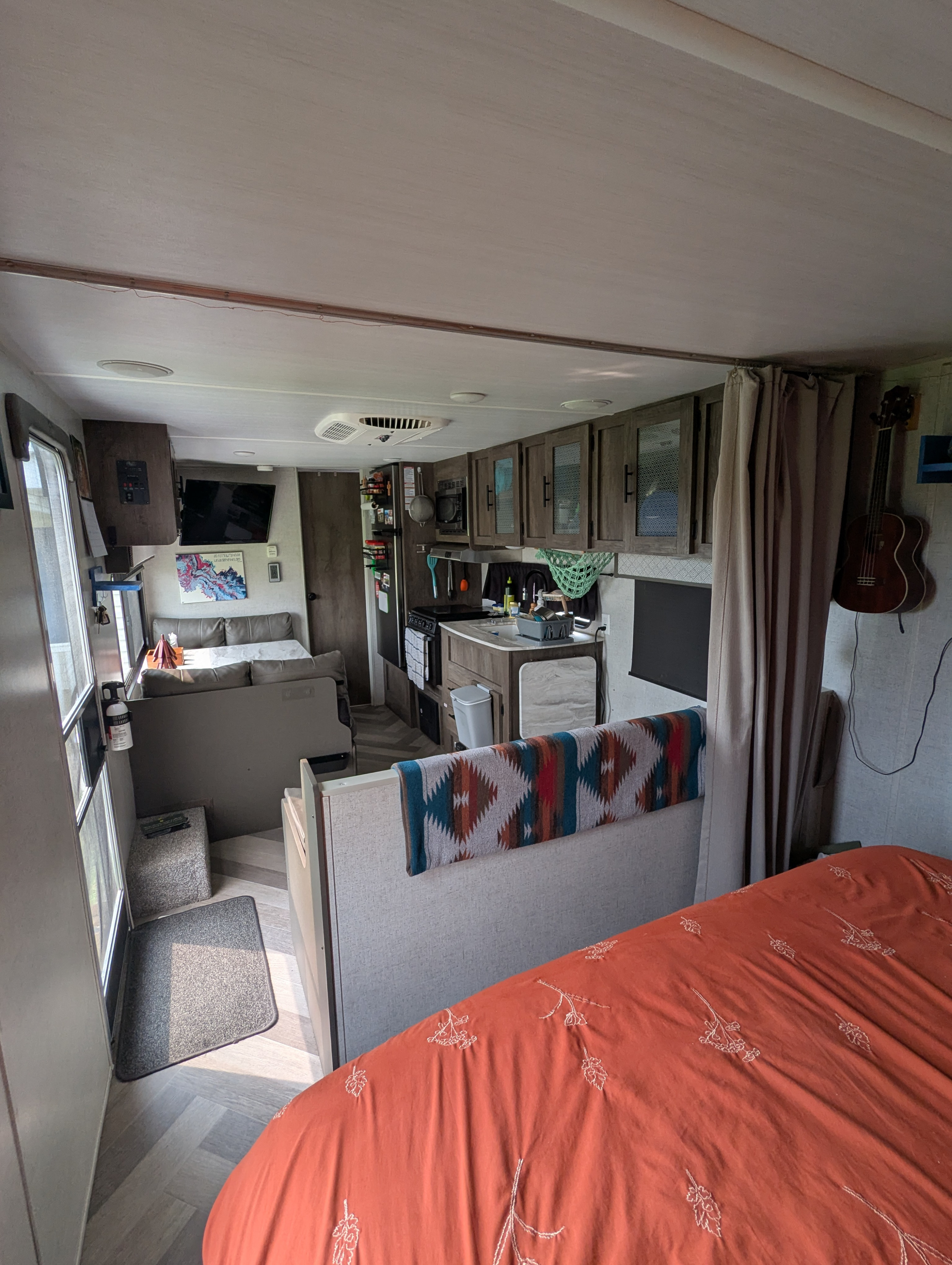View inside an RV rental, showing an orange bedspread in the foreground, leading to a living/dining area and a compact kitchen.. Forest River Salem Cruise Lite 2020