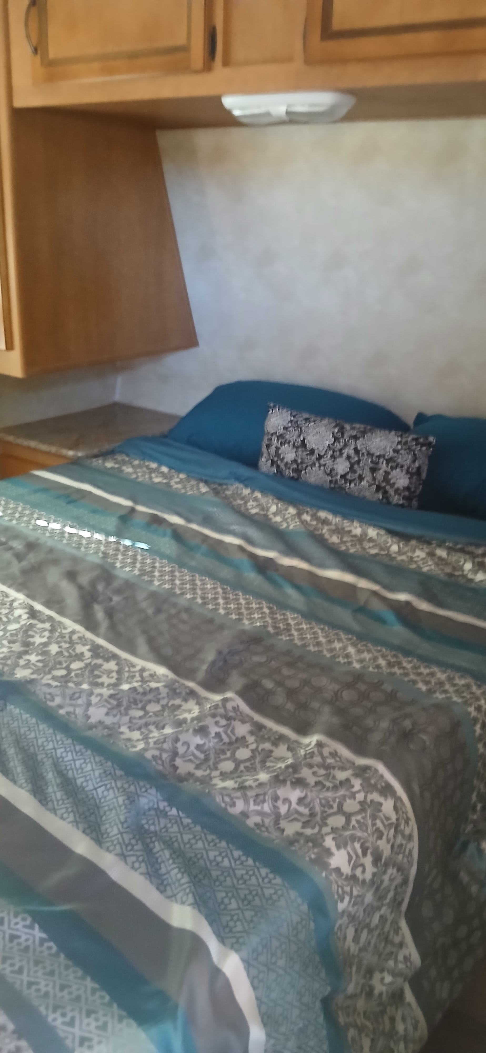 Cozy bedroom in an RV rental featuring blue and patterned bedding, wood cabinets, and a side counter.. Palomino Puma 2013
