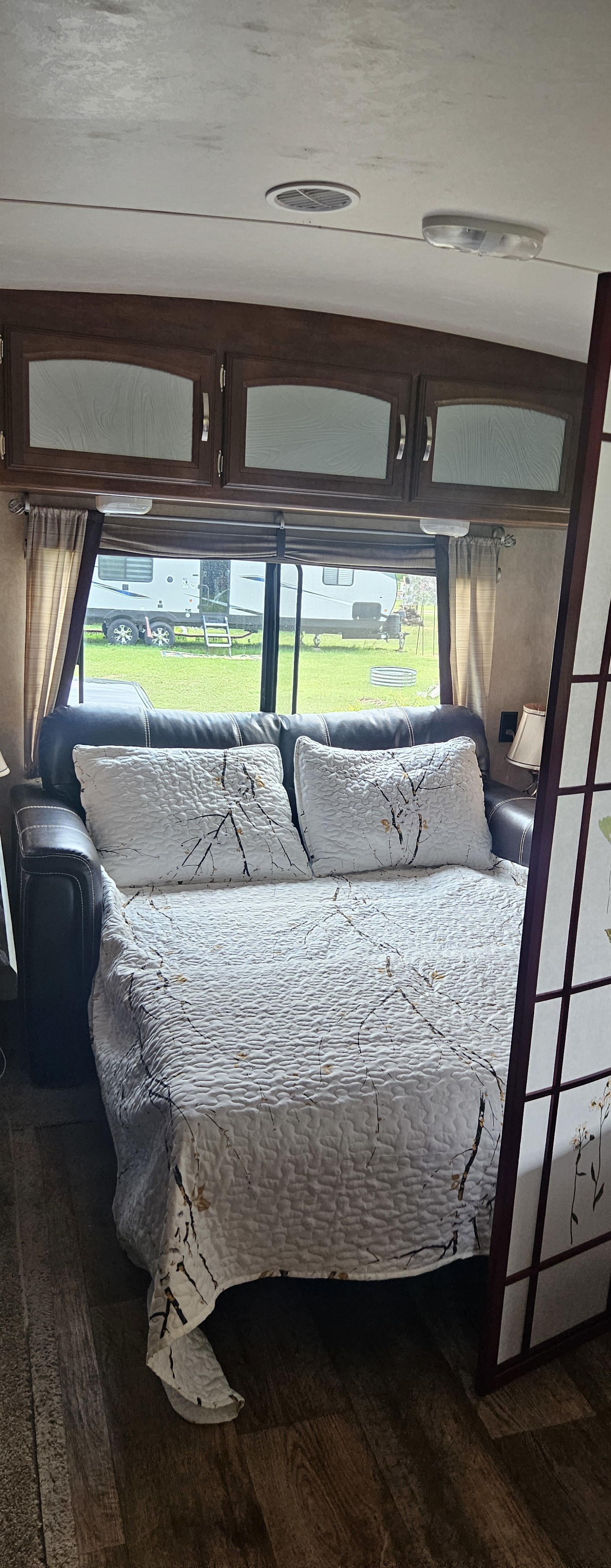 Inside this RV rental, a comfy sofa bed with a nature-themed quilt and pillows offers a relaxing space, featuring wood cabinets and a window view.. Forest River Salem 2016