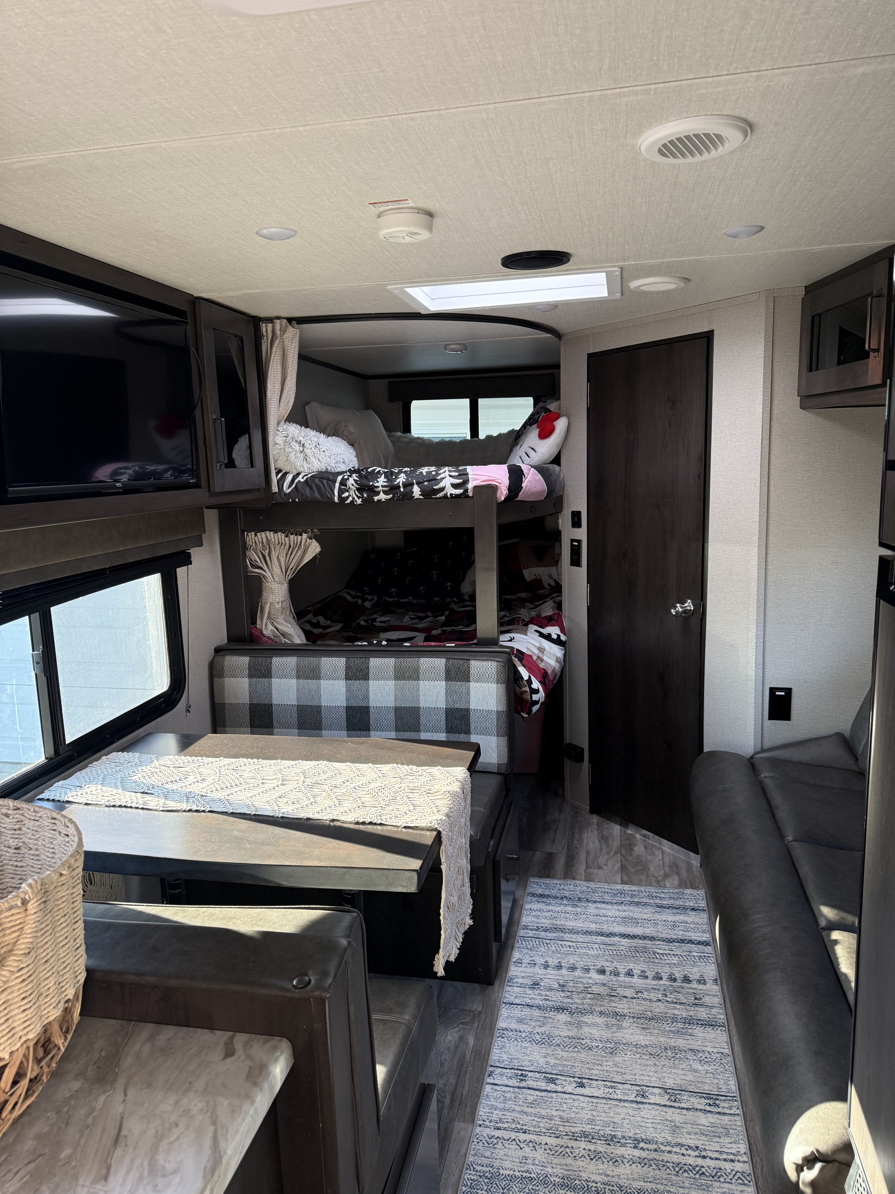 Cozy rv rental interior: bunk beds, dinette with plaid seating, sofa, and TV, perfect for a comfortable stay.. Grand Design Transcend Xplor 2023