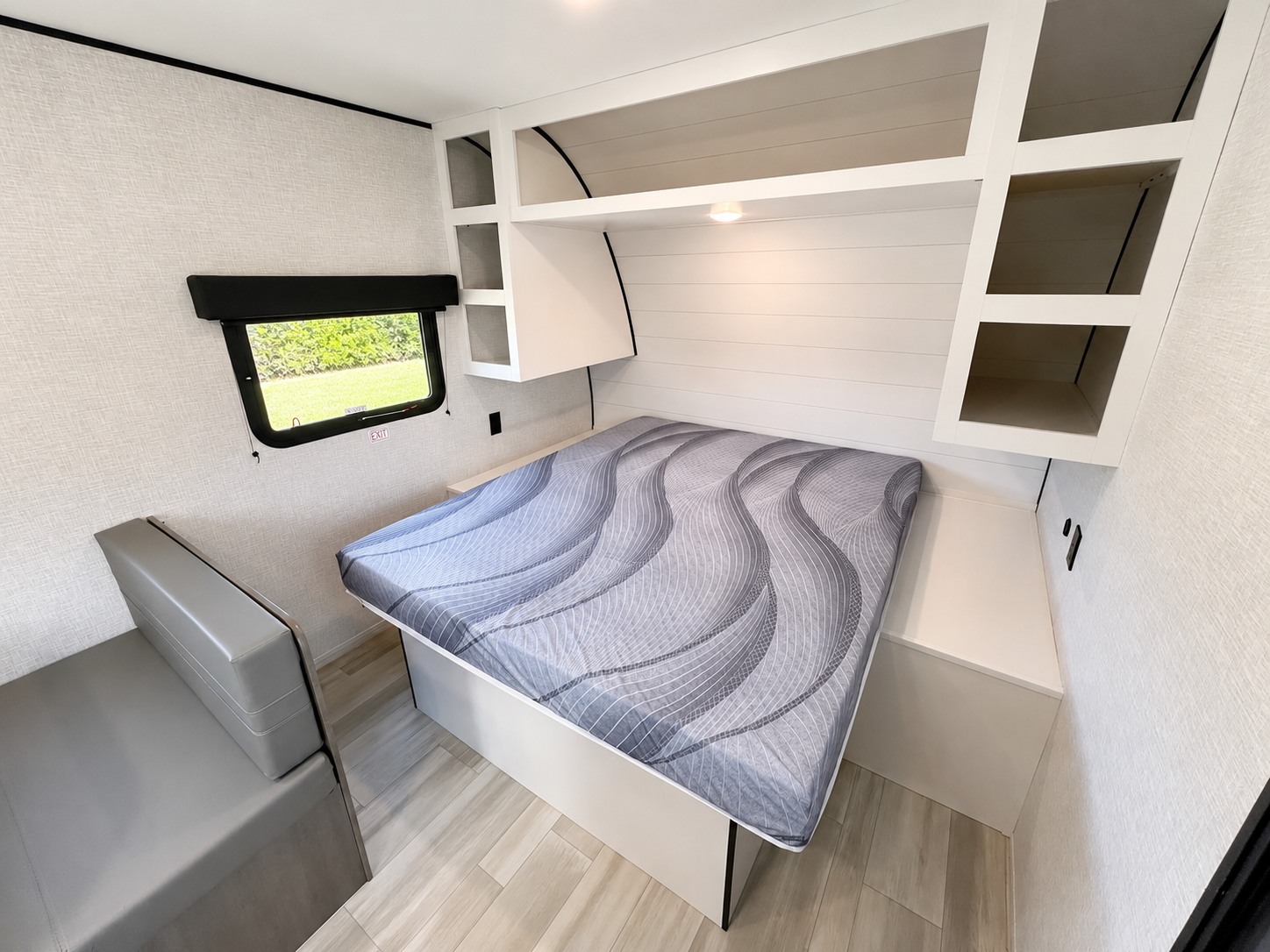 RV rental interior: a modern compact bedroom with a patterned bed, white overhead shelves, and a gray sofa by the window.. Starcraft AR-One 2025