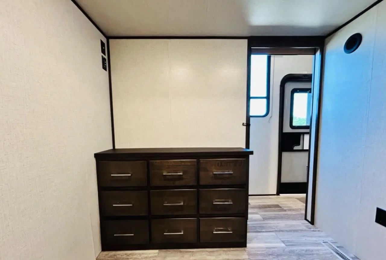 Spacious RV rental interior featuring a dark wooden dresser, light walls, and a visible passage to another area.. Dutchmen Triton 4271 2022