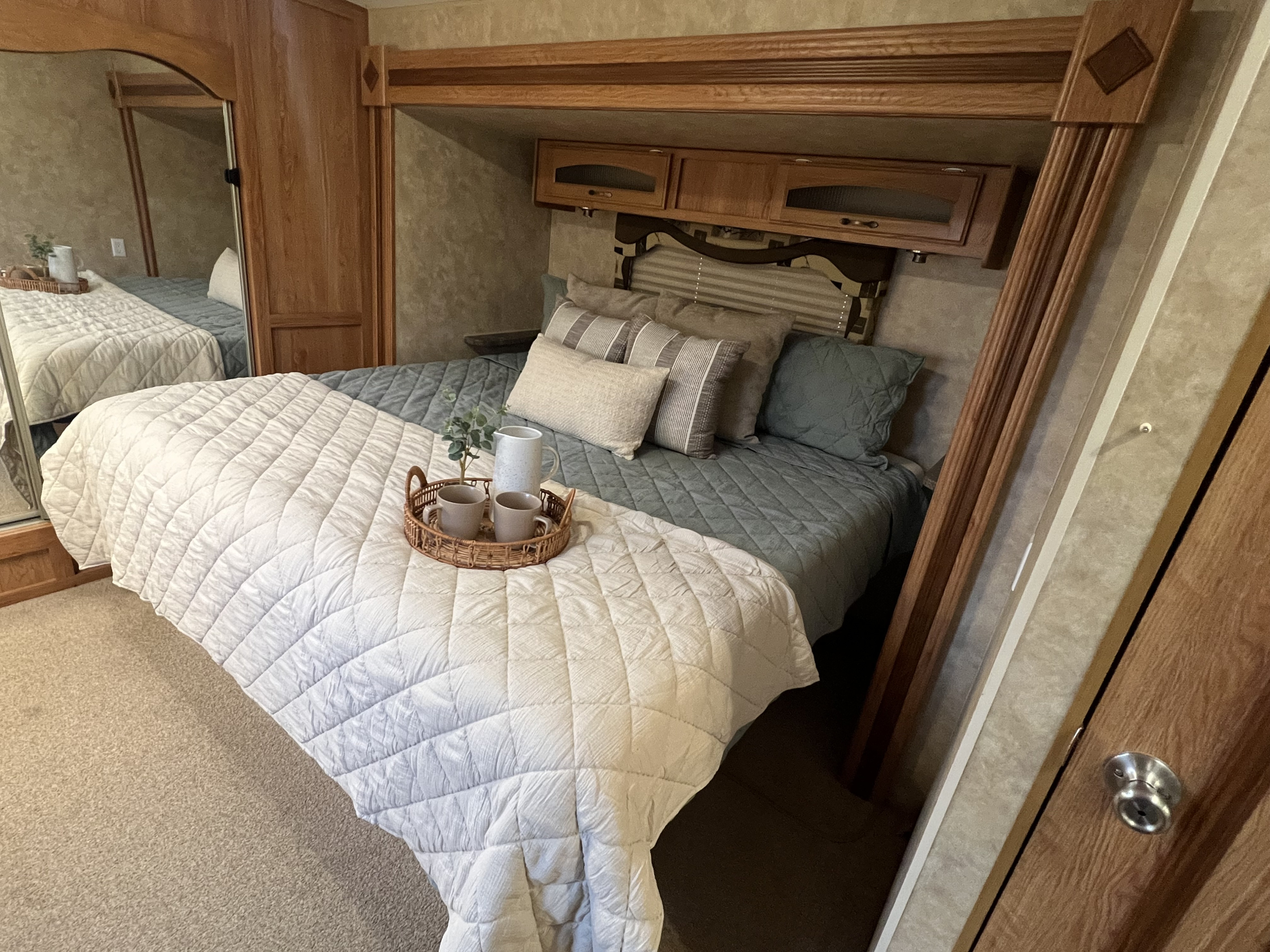 Cozy RV rental bedroom with plush quilted bedding, decorative pillows, overhead storage cabinets, and a charming bedside tray.. Jayco Eagle 2009
