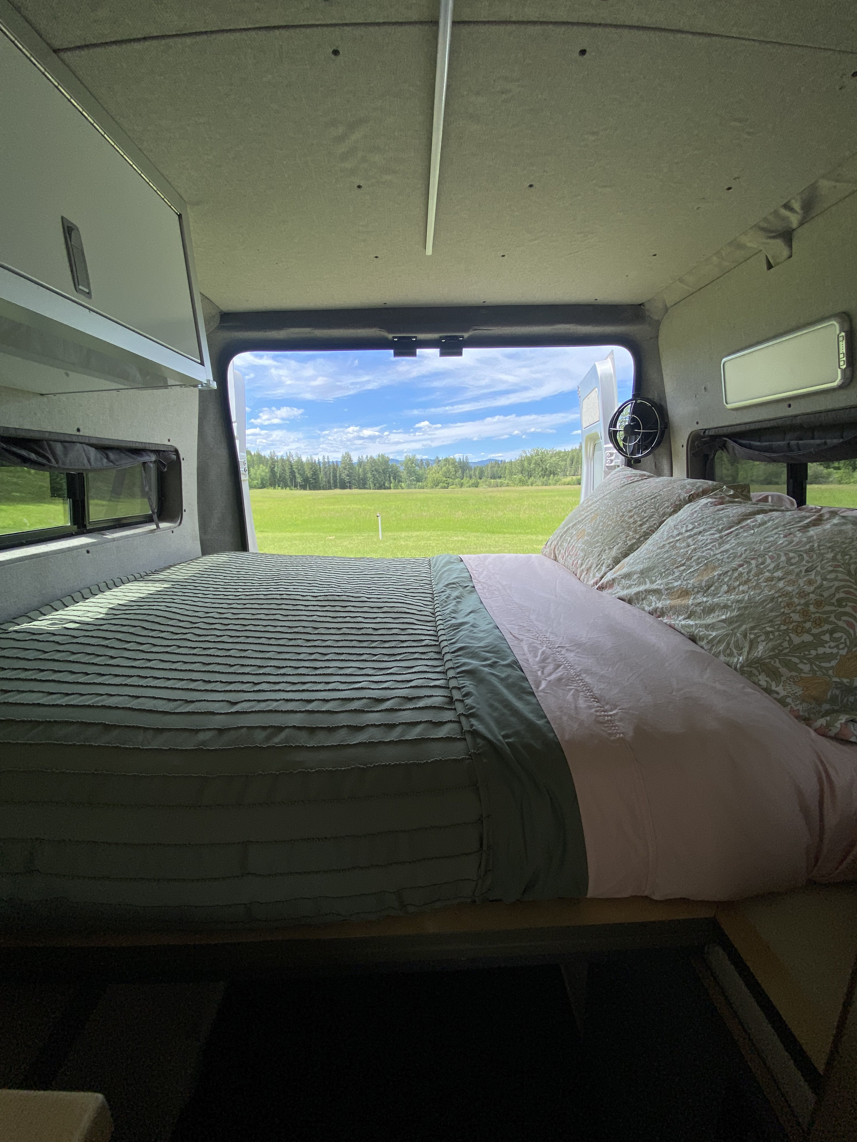 Cozy RV rental bedroom with a stunning view of a green field, forest, and blue sky from the open back doors.. Dodge Promaster 3500 2017