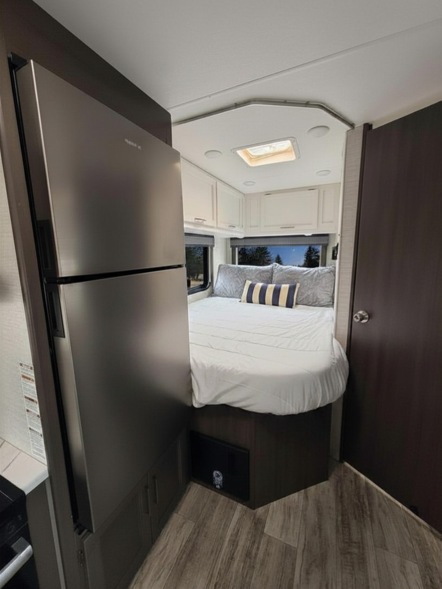 RV rental bedroom view: features a large bed with white linens, windows, overhead cabinets, and a modern tall refrigerator.. Thor Chateau 2024