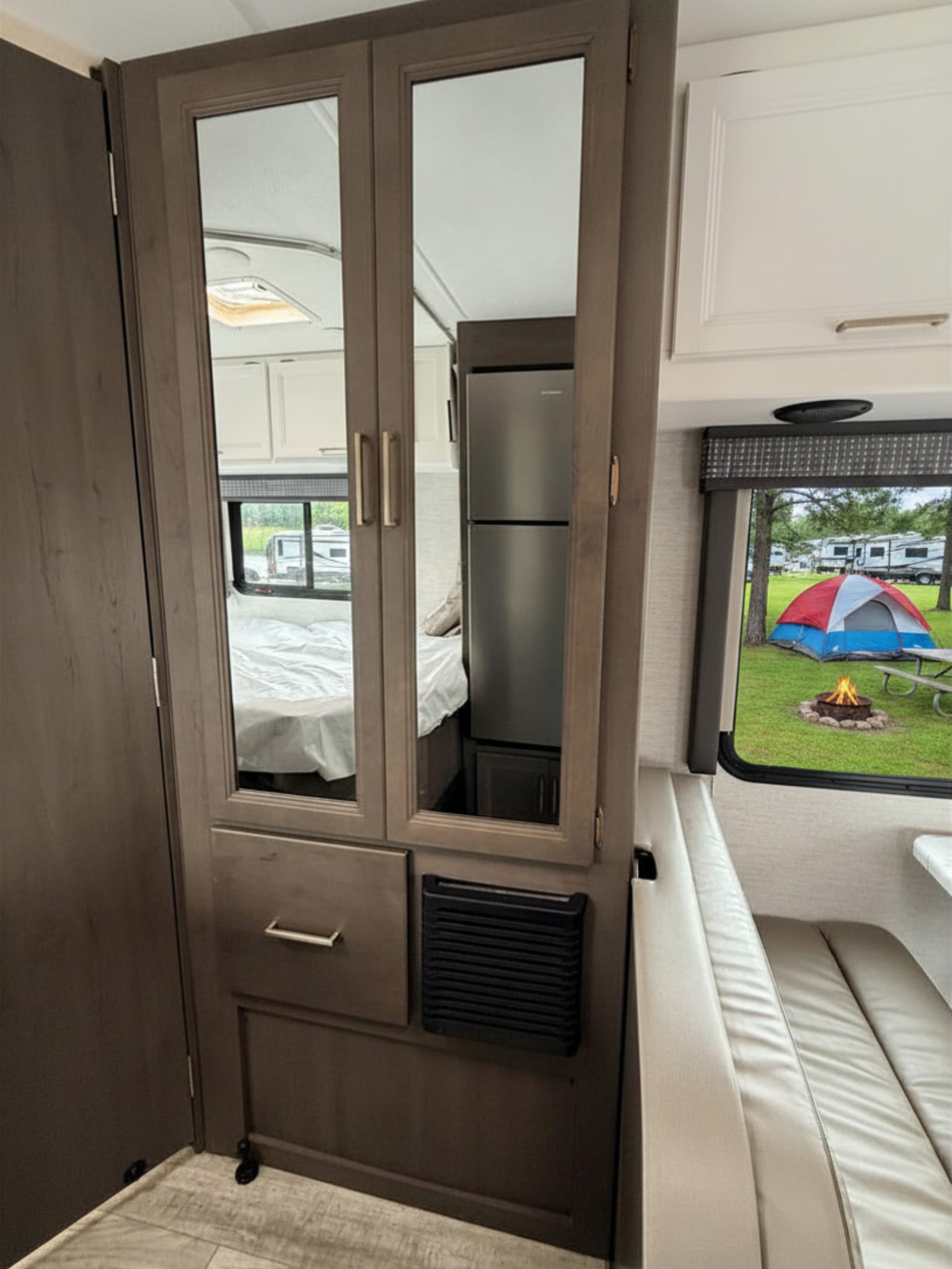 RV rental interior features a dinette, fridge, and mirrored closet reflecting the bedroom. Outside, a tent, campfire, and campsite.. Thor Chateau 2024