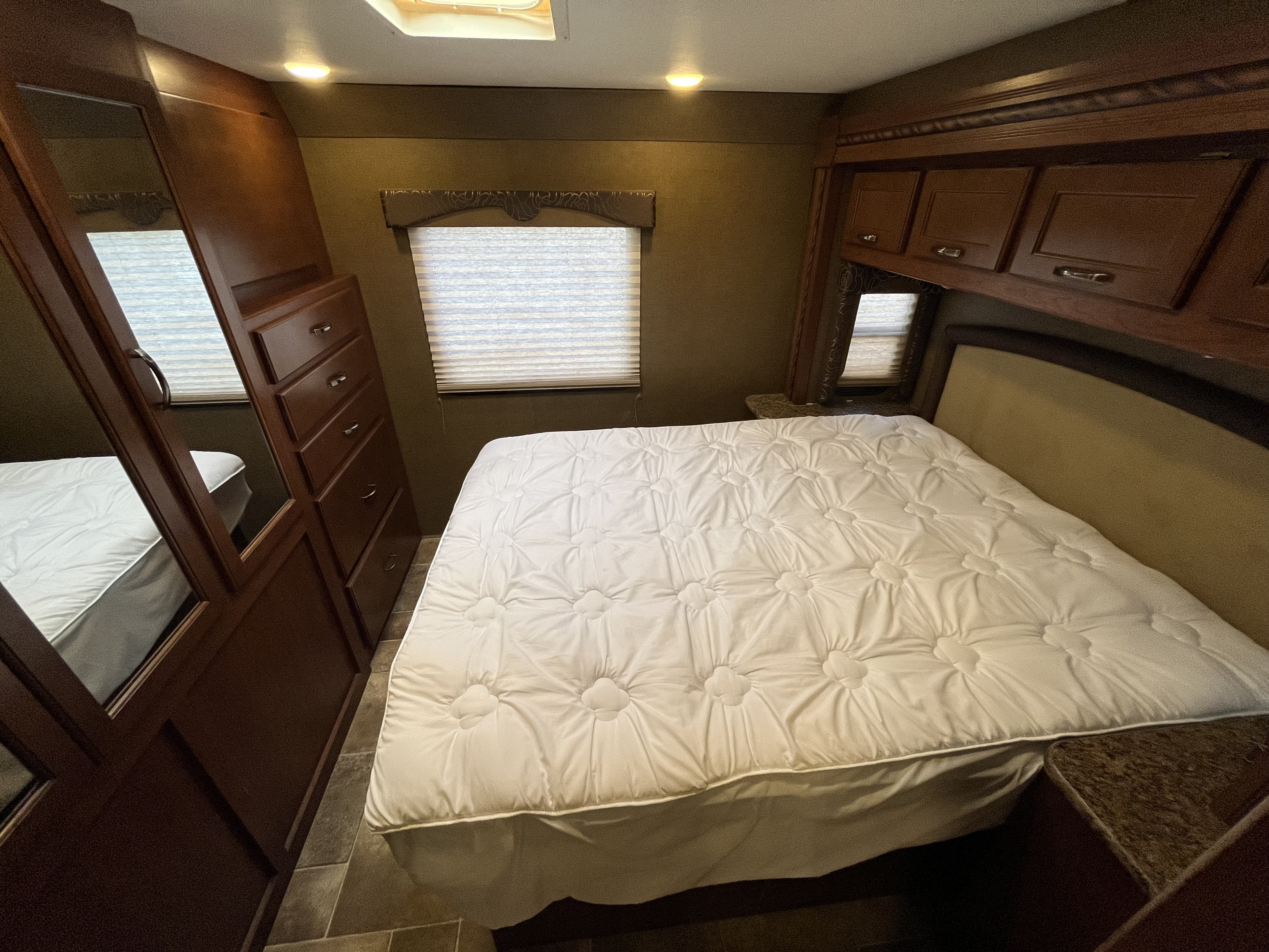 This RV rental bedroom features a comfy bed, rich wooden cabinets, and a mirrored wardrobe for a functional stay.. Thor Freedom Elite 2016