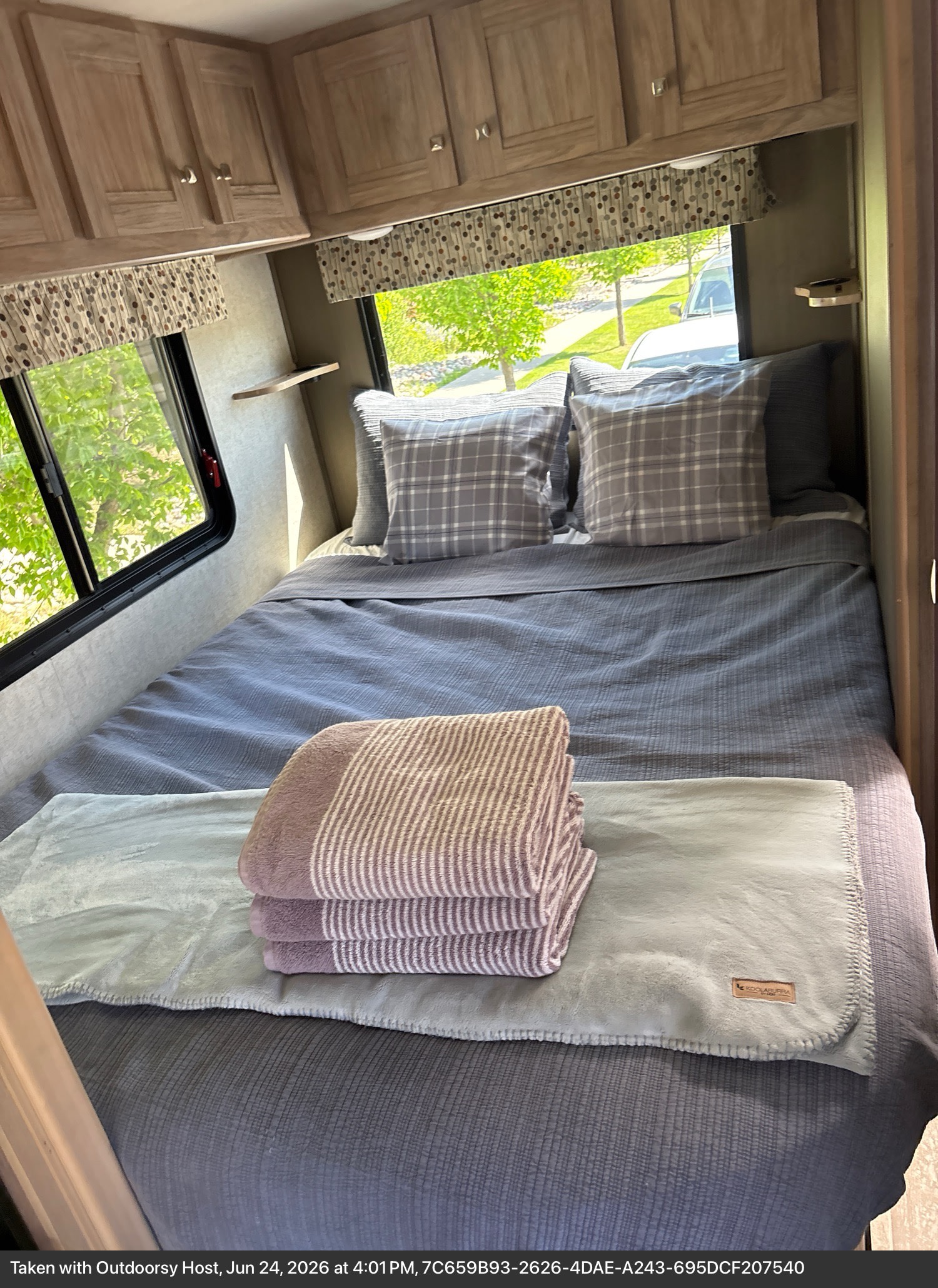 Cozy rv rental bedroom features a neatly made bed with blue bedding, plaid pillows, and stacked blankets, ideal for comfort.. Forest River Sunseeker LE 2020