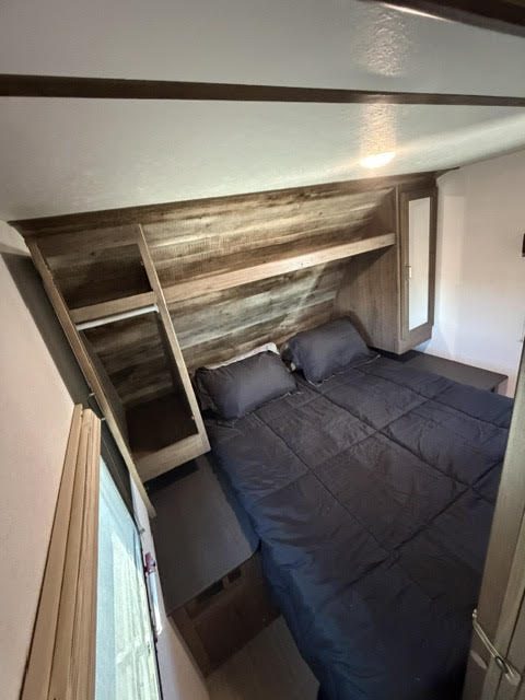 Cozy RV rental bedroom with a dark bed, wooden headboard shelves, and compact storage cabinets. Perfect for a comfortable stay on the road.. Keystone RV Passport Ultra Lite 2019