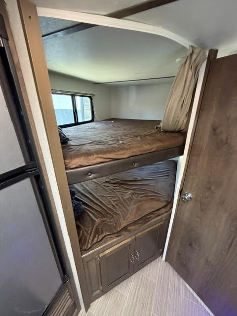 Inside an RV rental: two bunk beds with brown sheets, bottom storage, and a window for natural light.. Keystone RV Passport Ultra Lite 2019