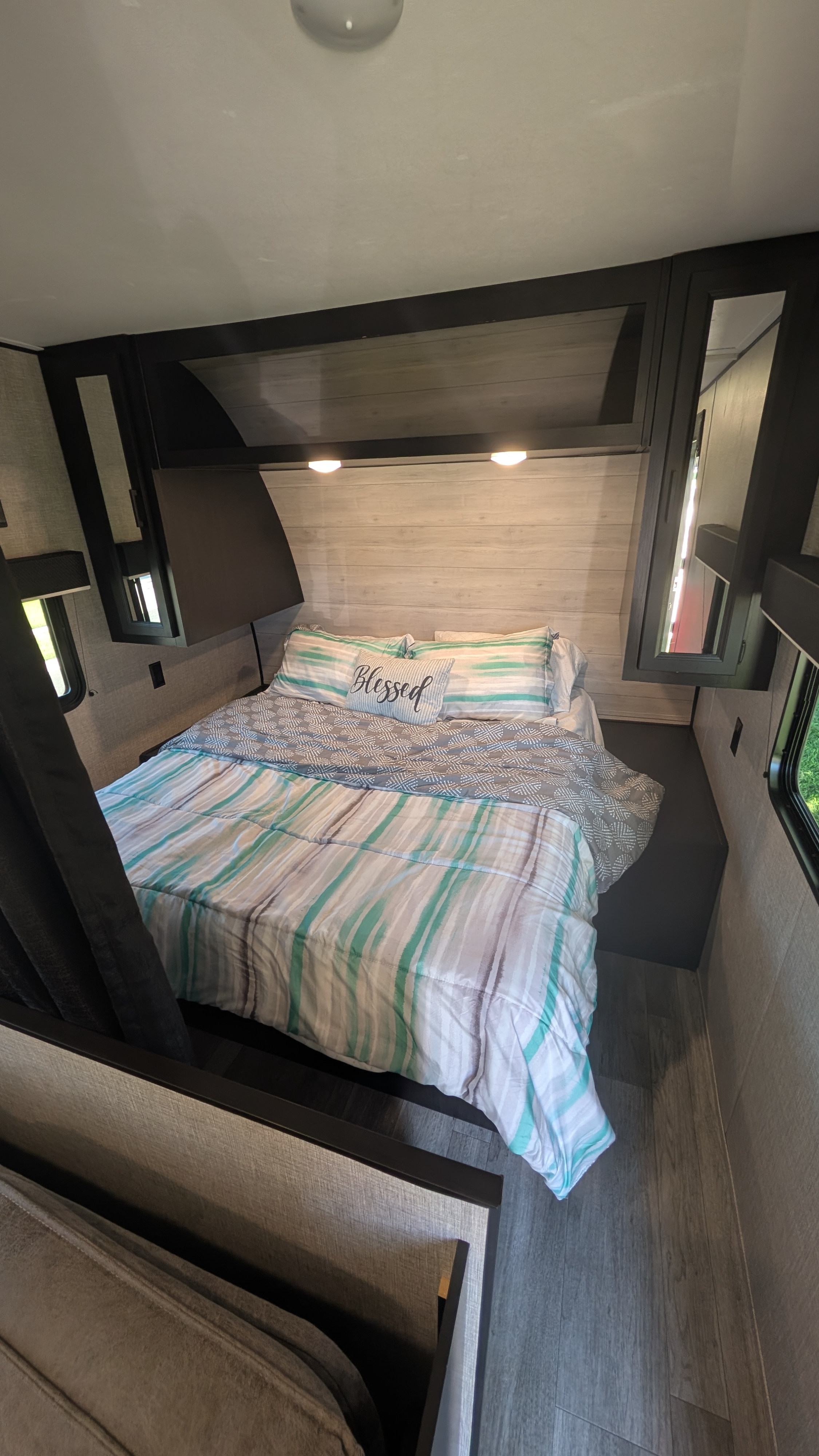 This cozy RV rental bedroom offers a comfortable bed with striped bedding, "Blessed" pillow, storage, and windows for your travels.. Jayco Jay Flight SLX 2023