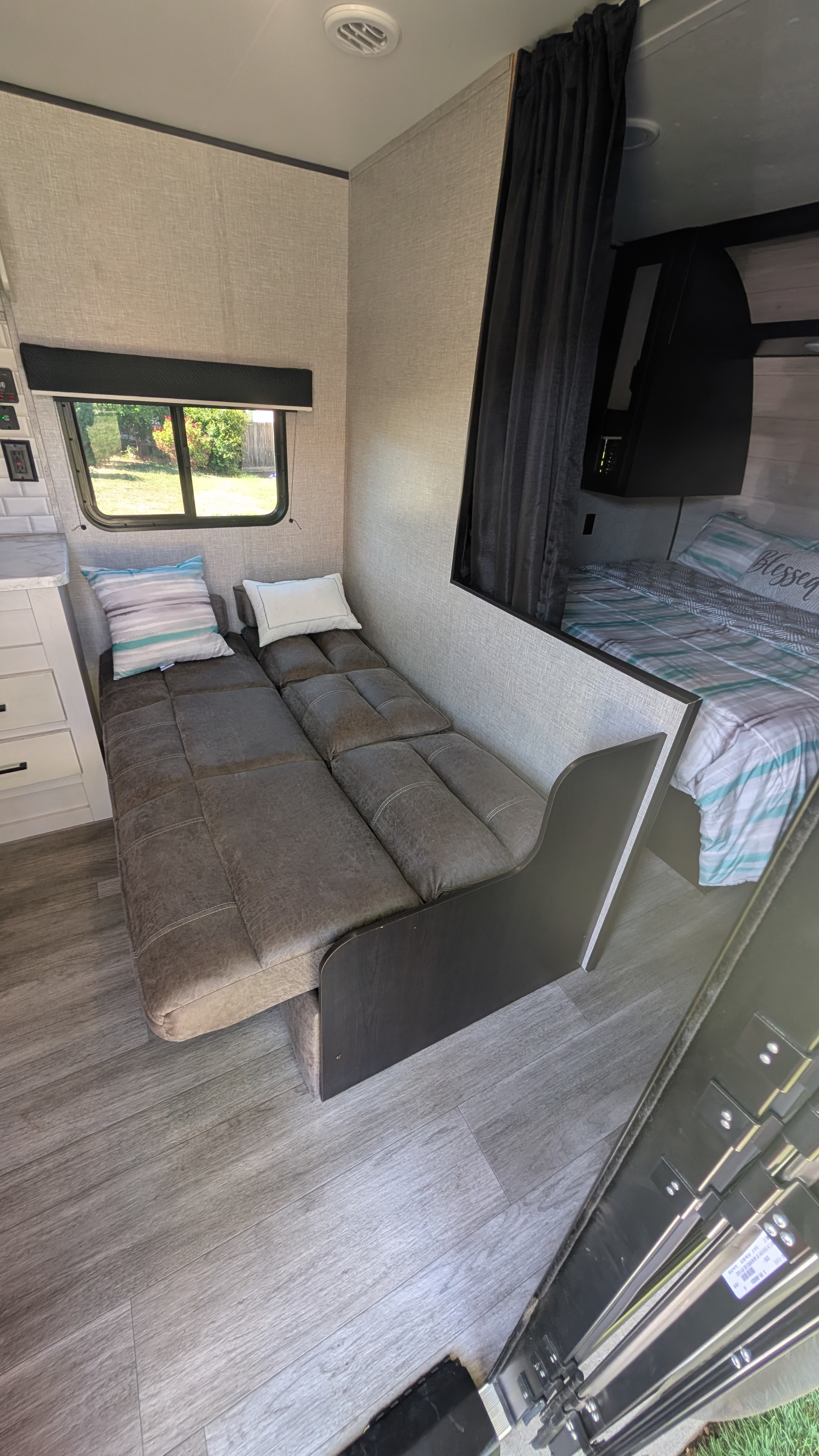 Compact RV rental interior featuring a versatile sofa bed, bright window, and a private bedroom space beyond the curtain.. Jayco Jay Flight SLX 2023