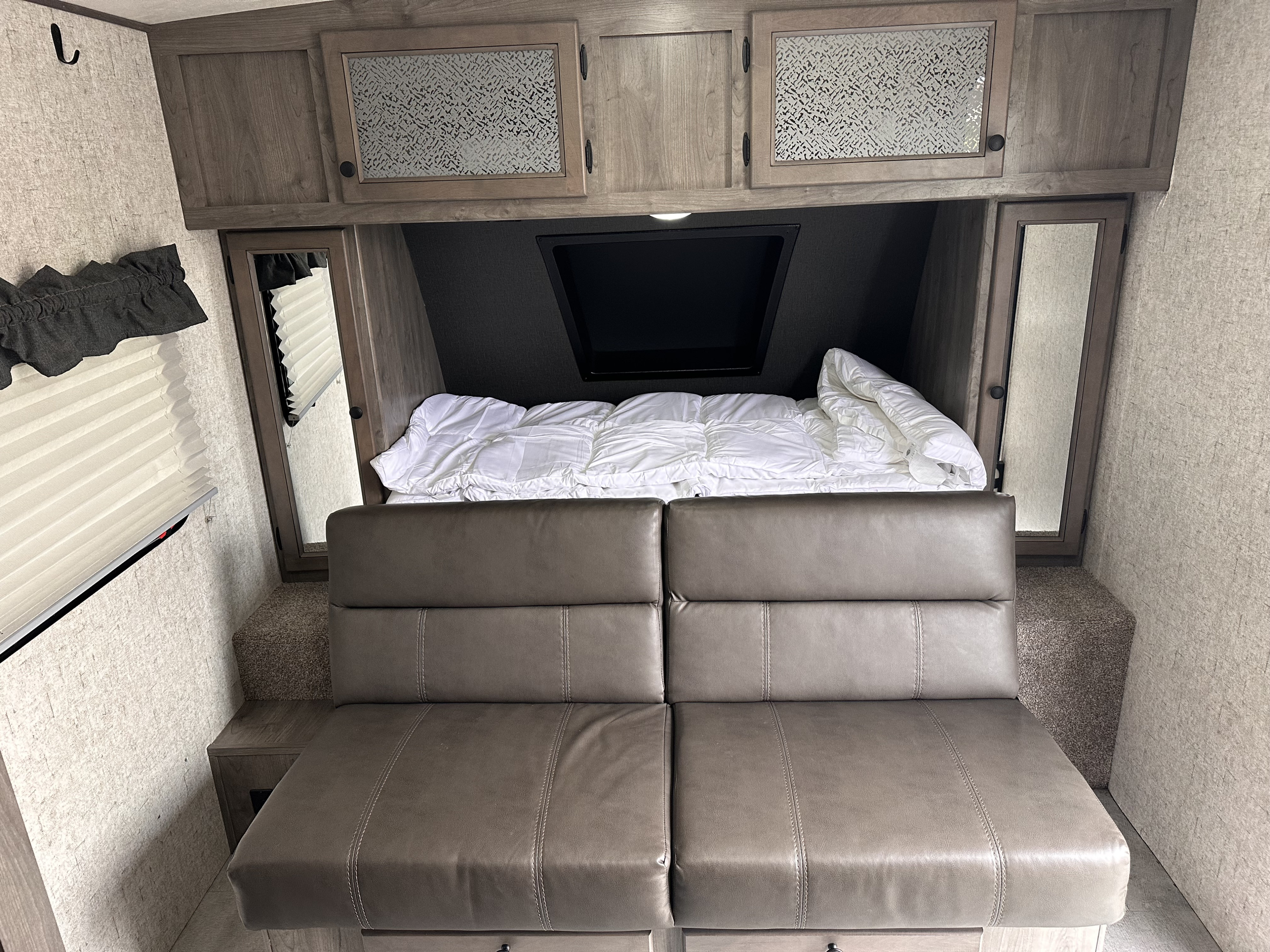RV rental interior: cozy sofa bed area with grey leather cushions, overhead storage, window, and a TV for camper comfort.. Coachmen Apex Nano 2020