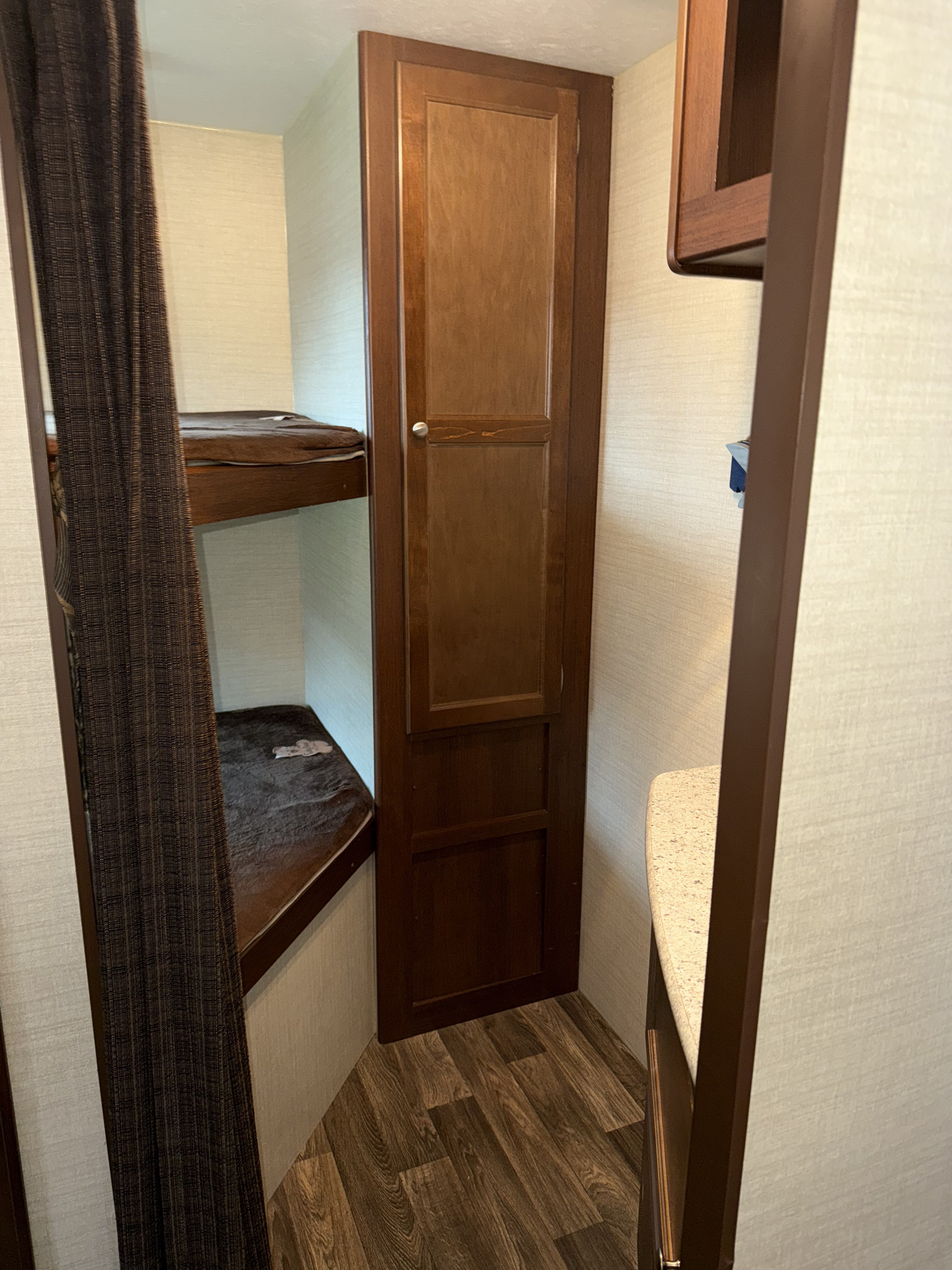 Compact RV rental interior: bunk beds with a dark curtain, a wood cabinet, and a light countertop.. Keystone RV Bullet Ultra Lite 2016